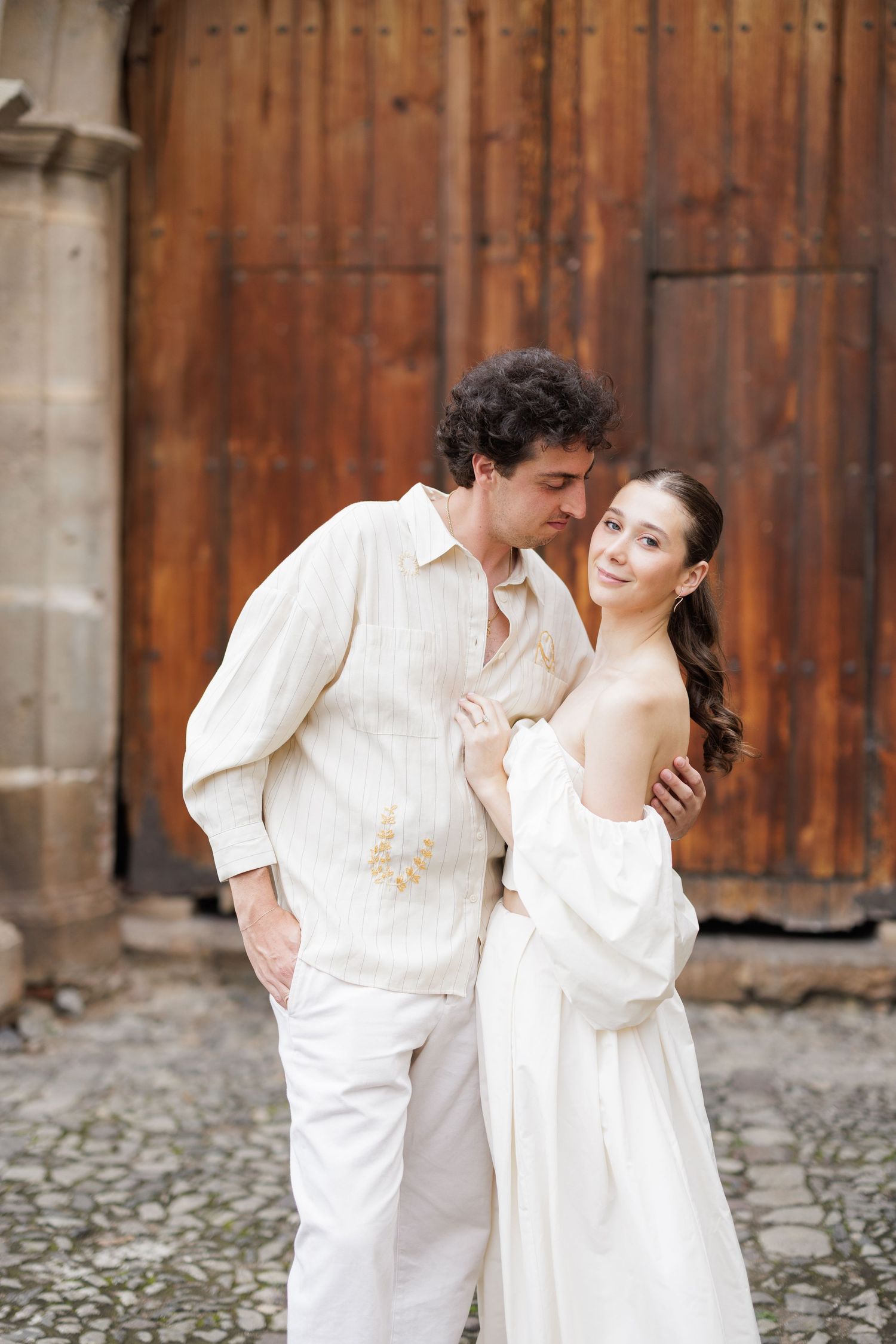 Romantic couple in white clothing posing against vintage wooden doors.