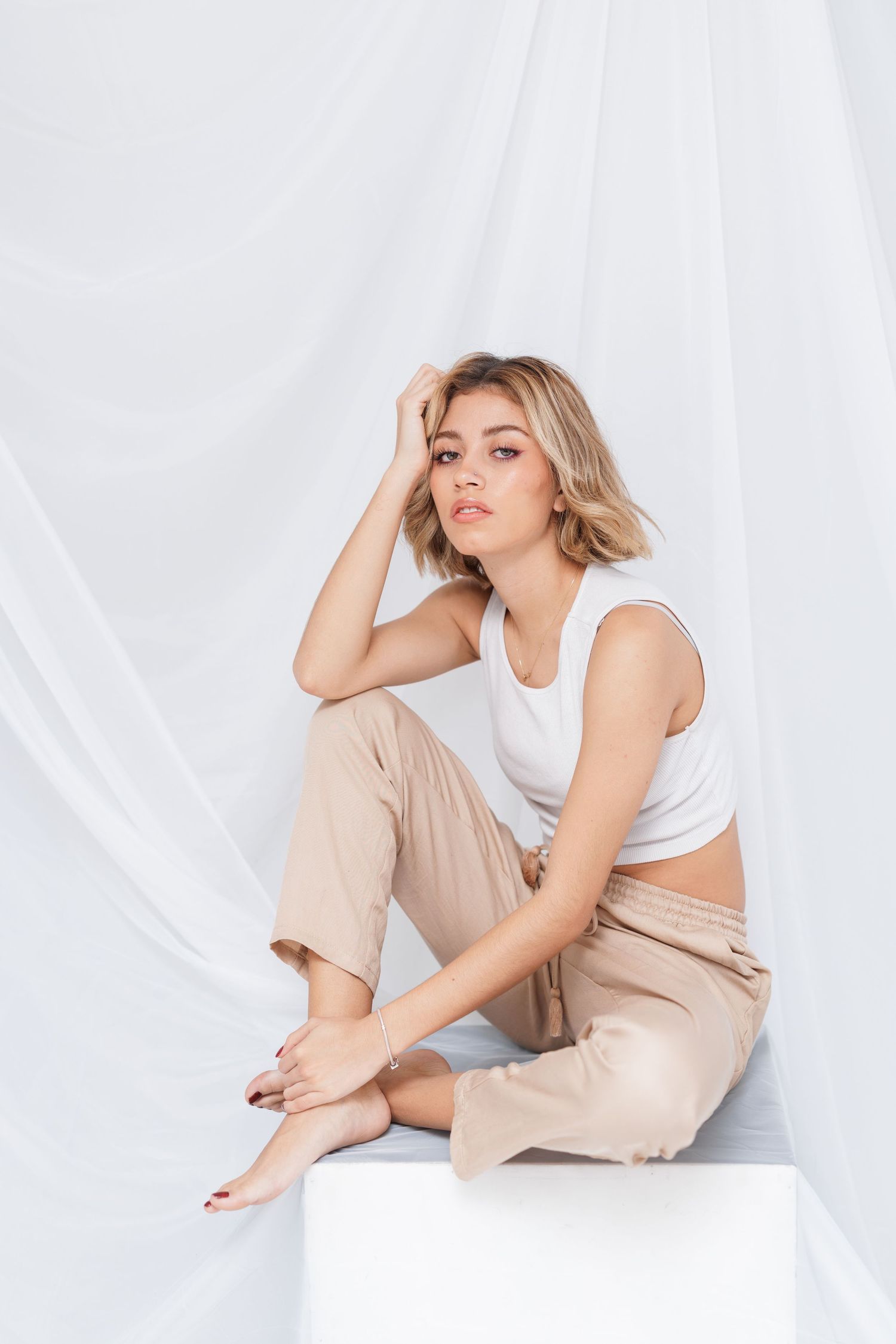 Fashion model poses in casual white top and beige pants against light background.