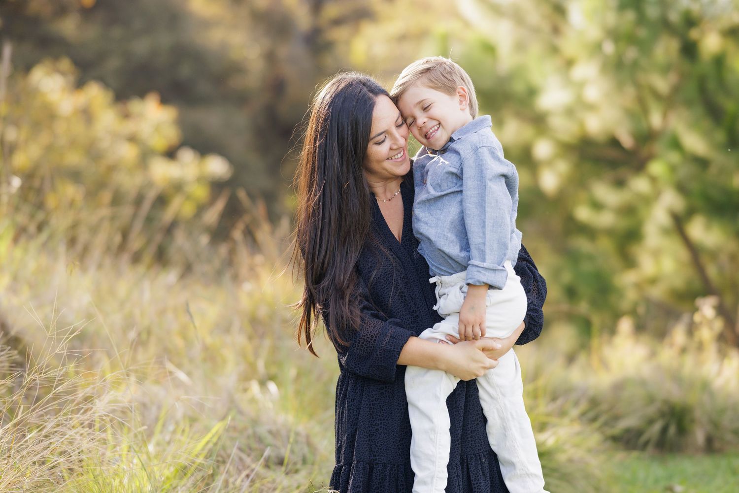 Mother and young child share a joyful embrace outdoors in autumn setting.