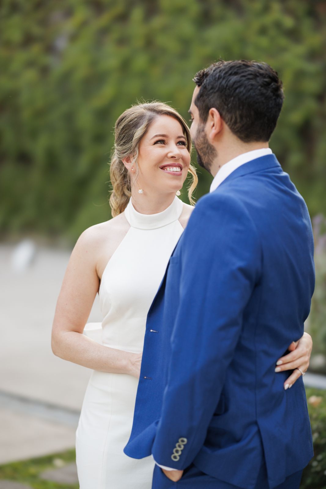 Romantic couple in white dress and blue suit share intimate moment in garden setting.