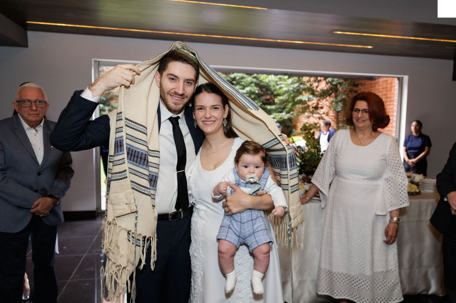 Jewish wedding ceremony with couple and baby under traditional prayer shawl.