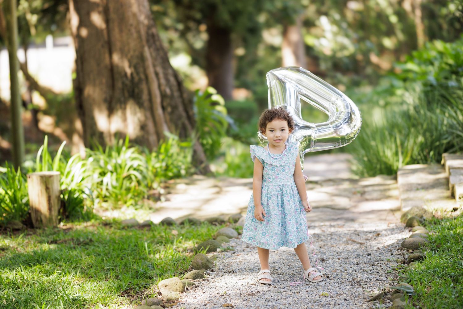 A child in a blue dress walks on a garden path with a silver balloon.