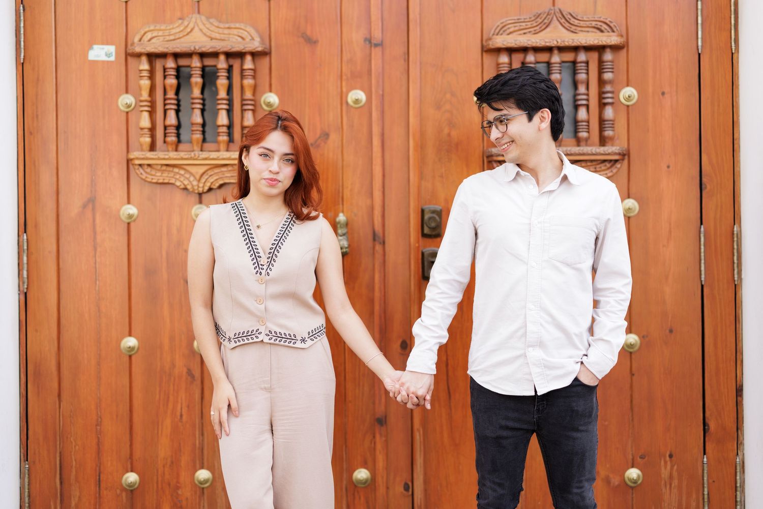 Couple in light colored outfits poses against rustic wooden door background.