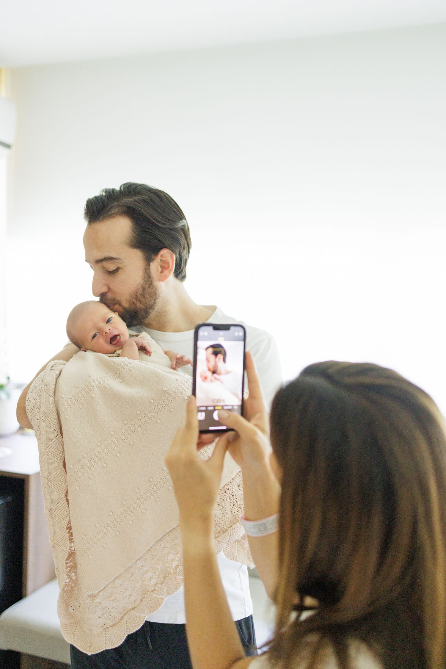 Someone taking photos of a special moment with a baby in cream-colored clothing.
