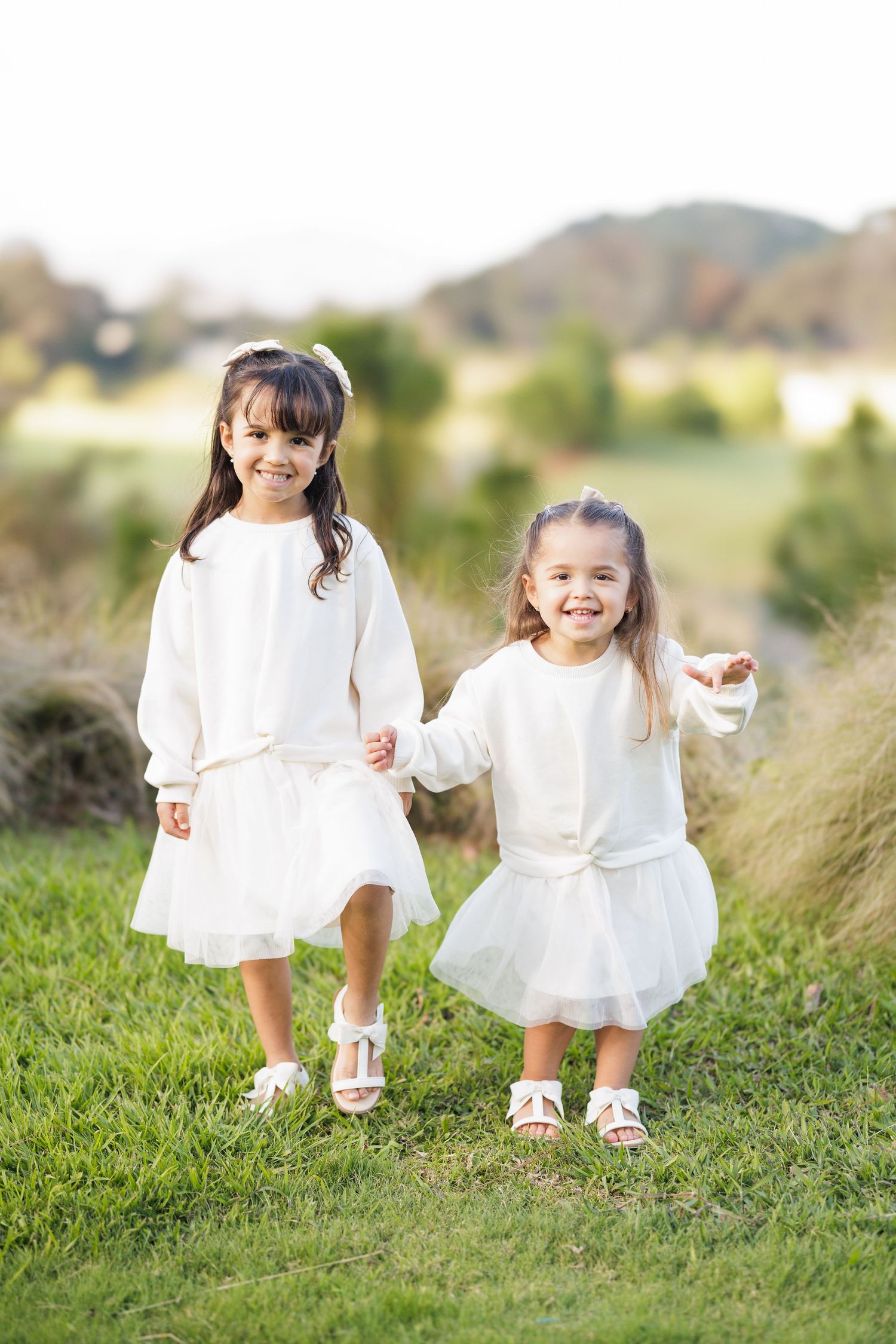 Children in white dresses running and playing on grassy hillside during golden hour.