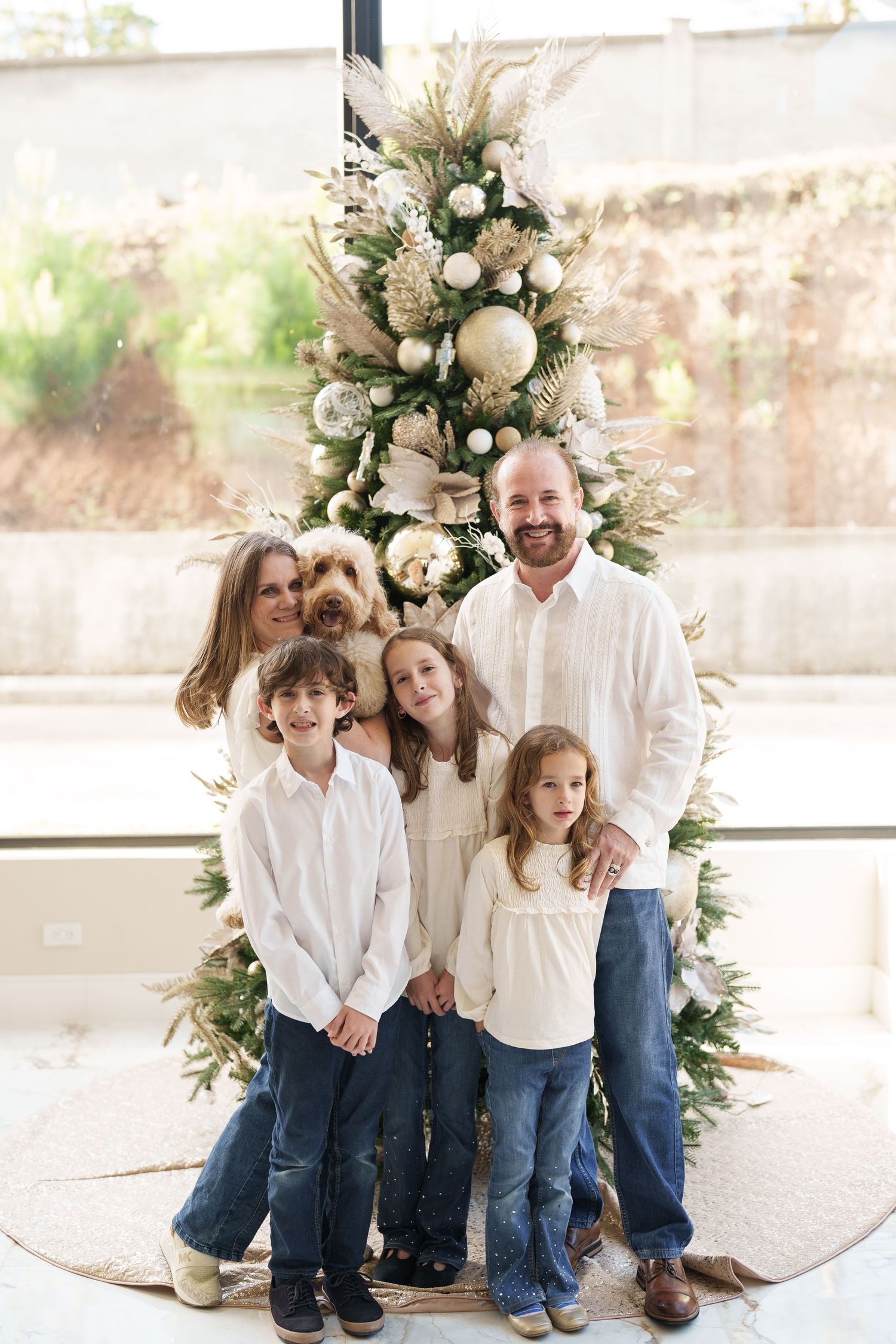 A family poses in front of an elegant Christmas tree decorated with white and gold ornaments.