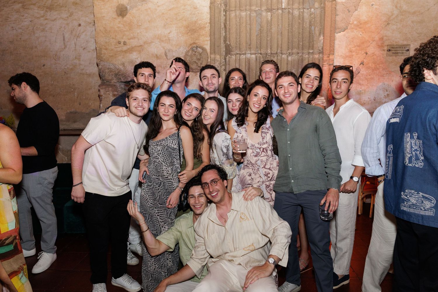 Group photo of party guests gathered in historic stone venue during evening celebration.