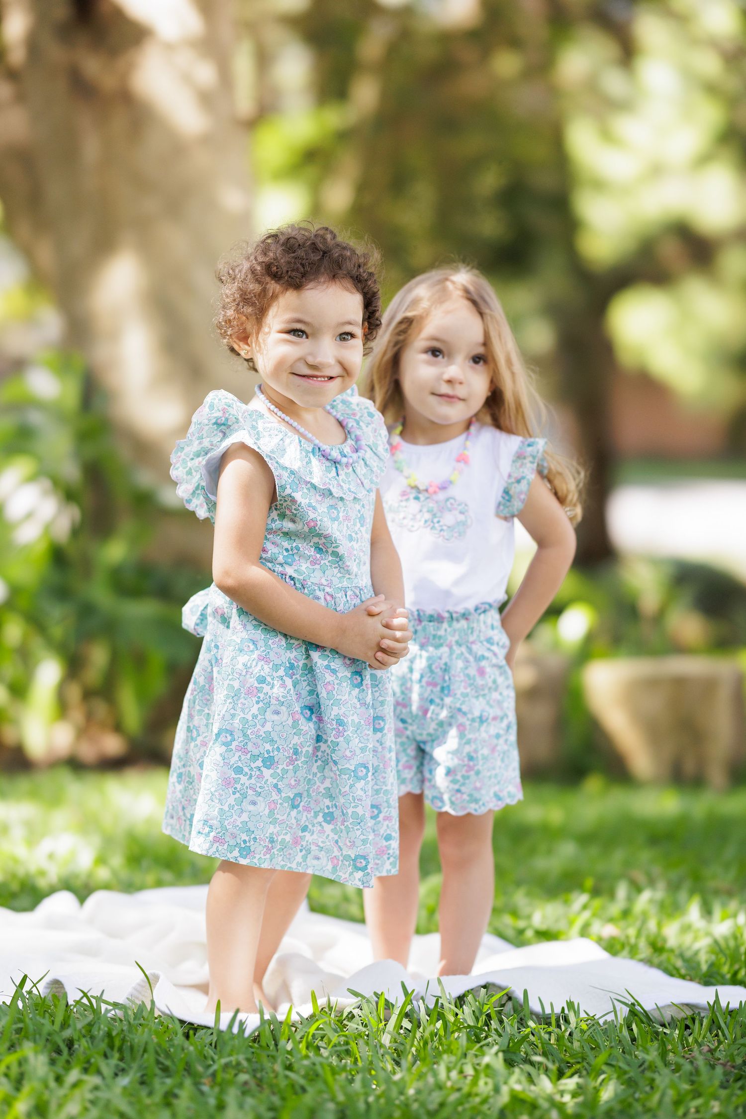 Young children in coordinated blue floral dresses play together on grass.