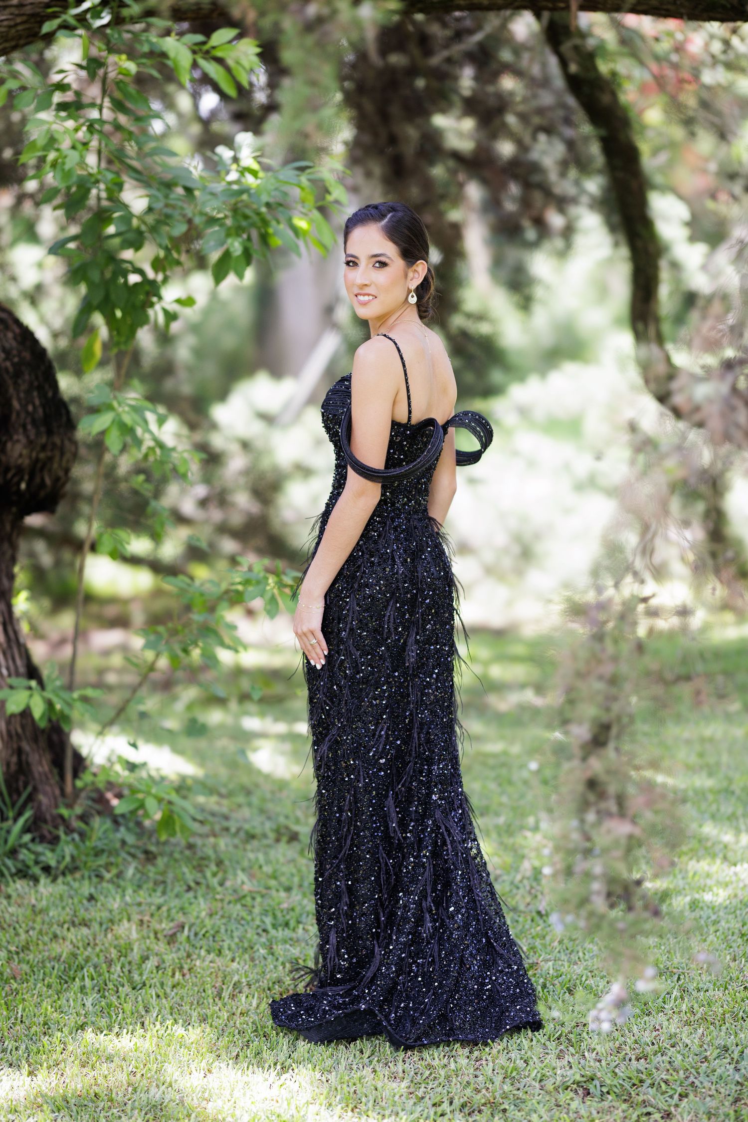 Woman in a sparkly navy blue formal dress poses outdoors in a garden setting.