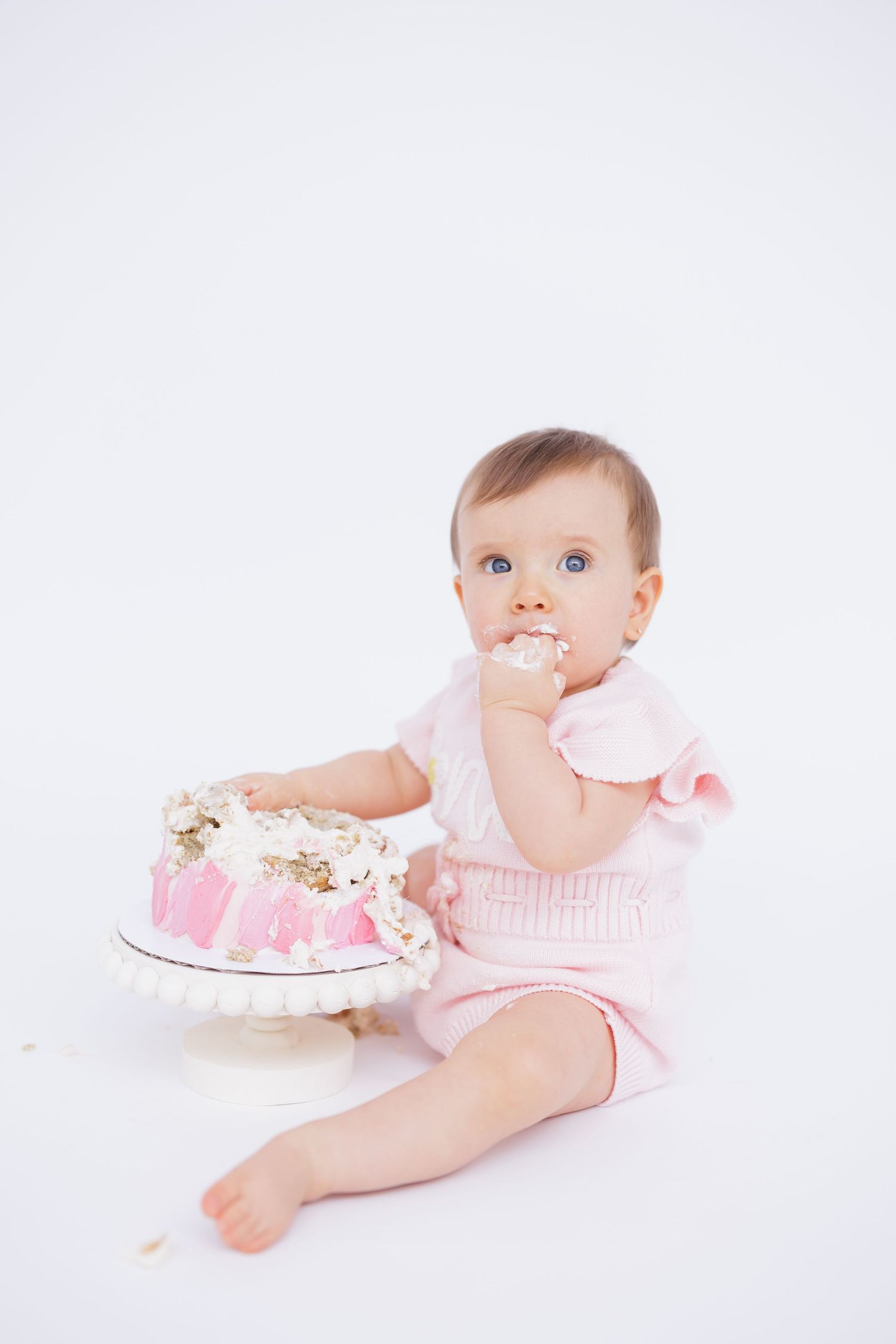 Baby in pink outfit crawling near decorated cake during cake smash photo session.