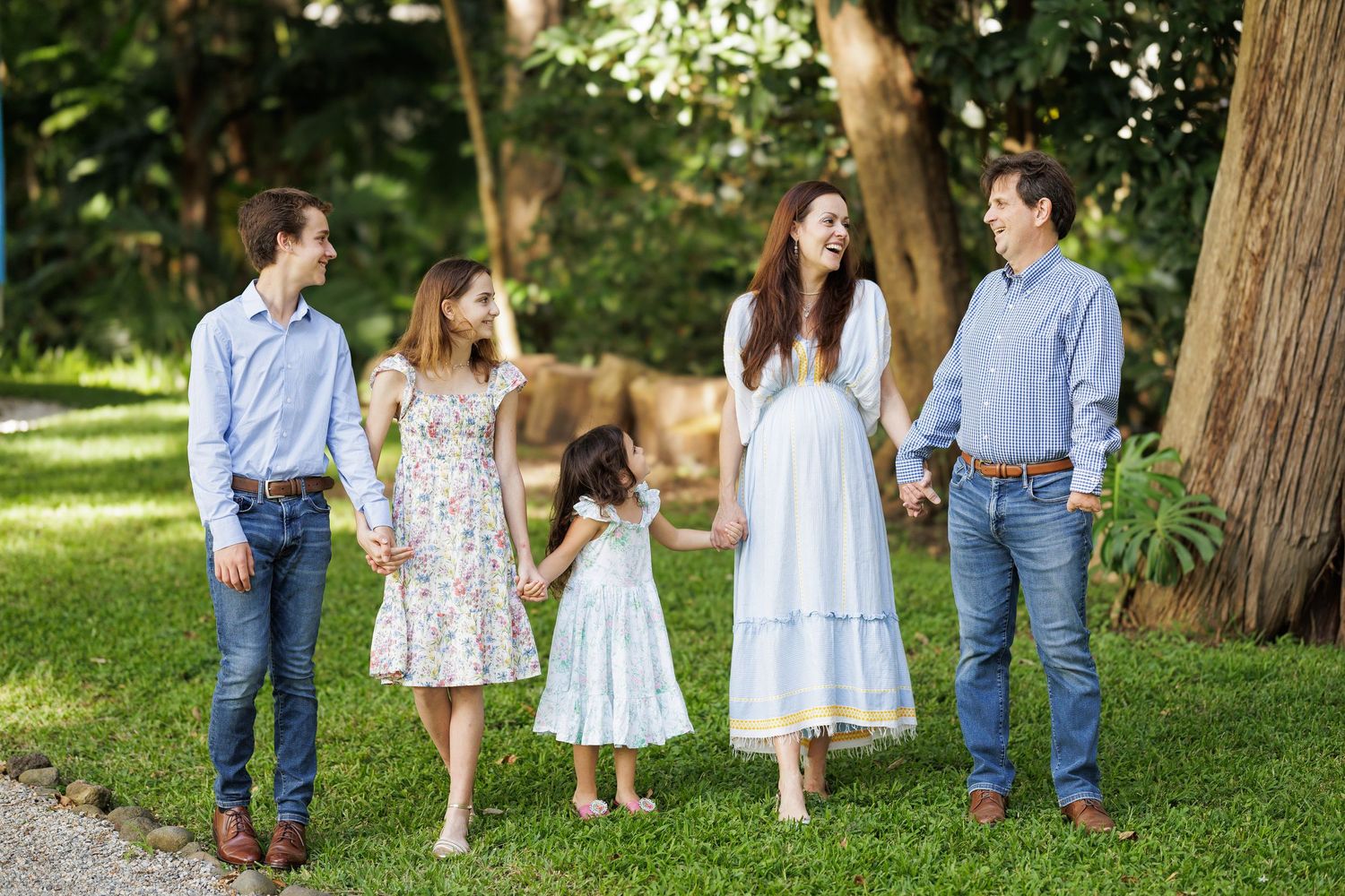 Family walking together through a wooded garden path on a sunny day.