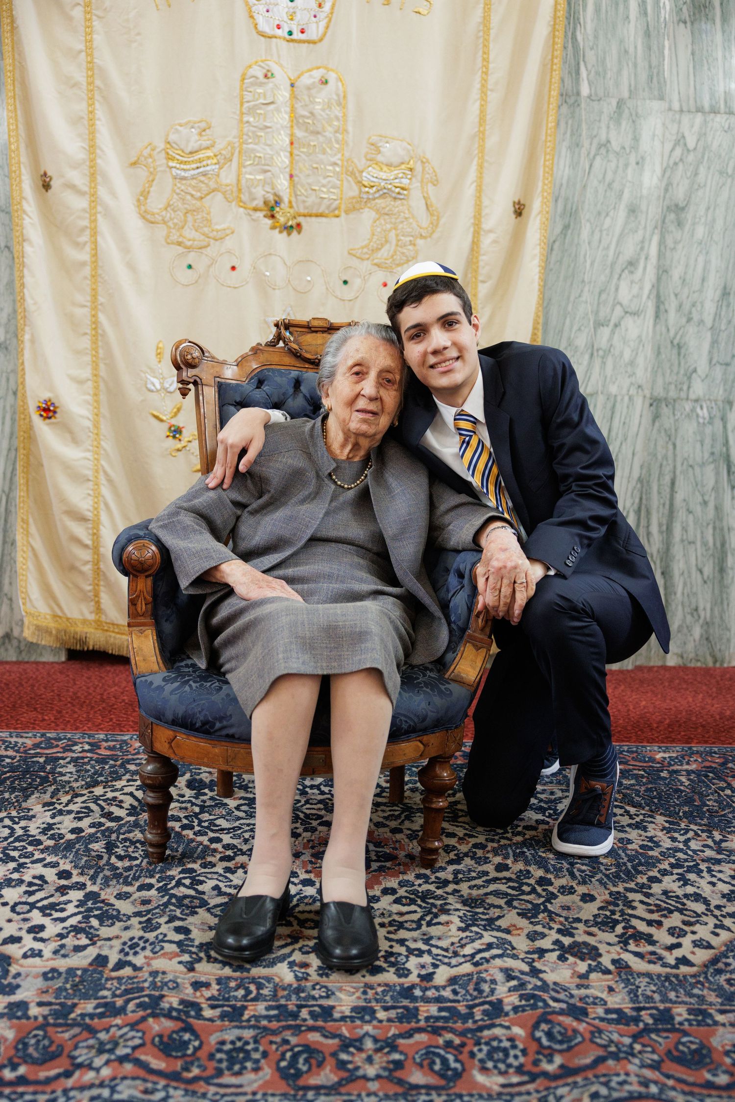 A sweet candid moment showing three generations sitting together on a bench at a formal event.