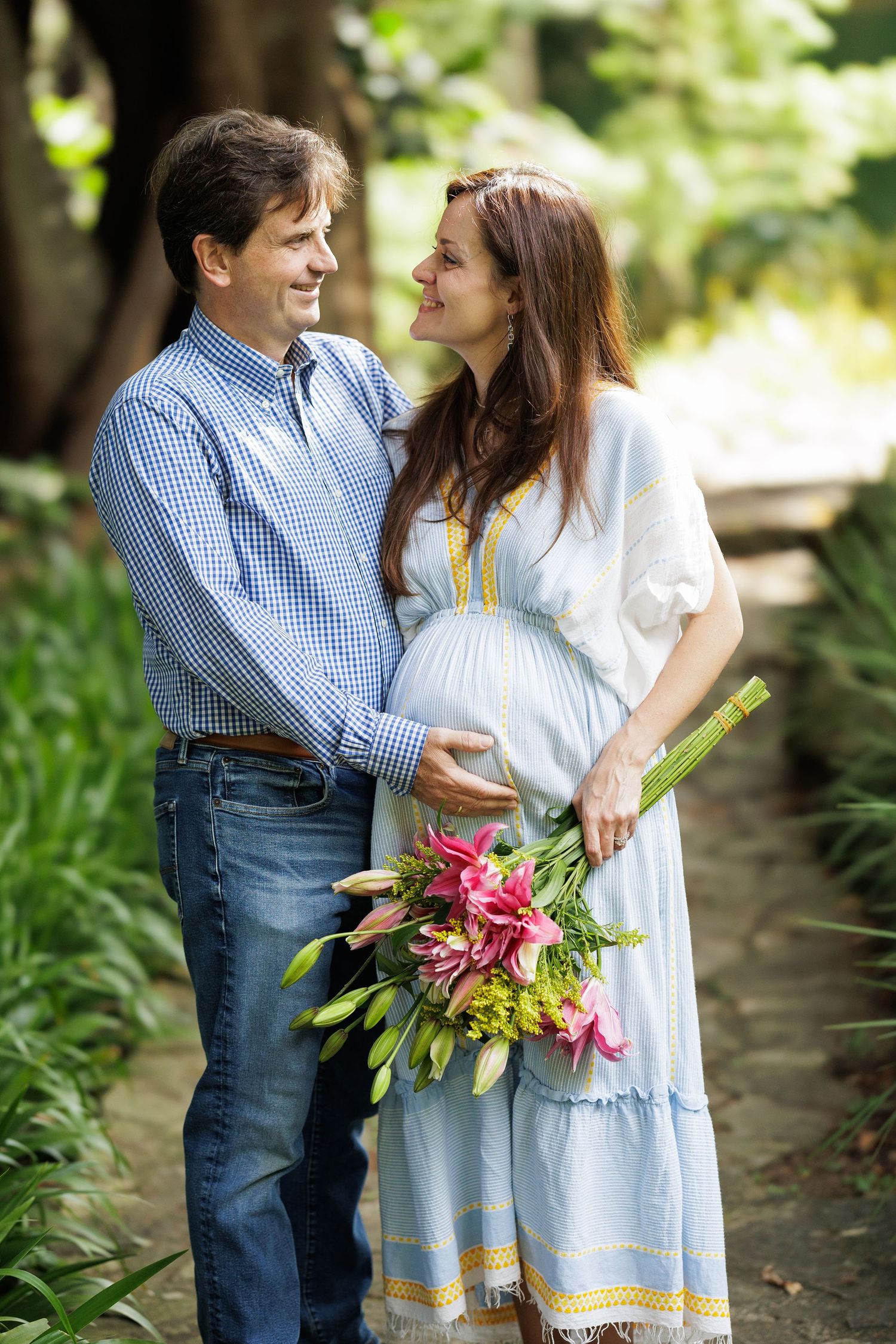 Couple poses with floral bouquet in garden setting wearing coordinated blue and white outfits.