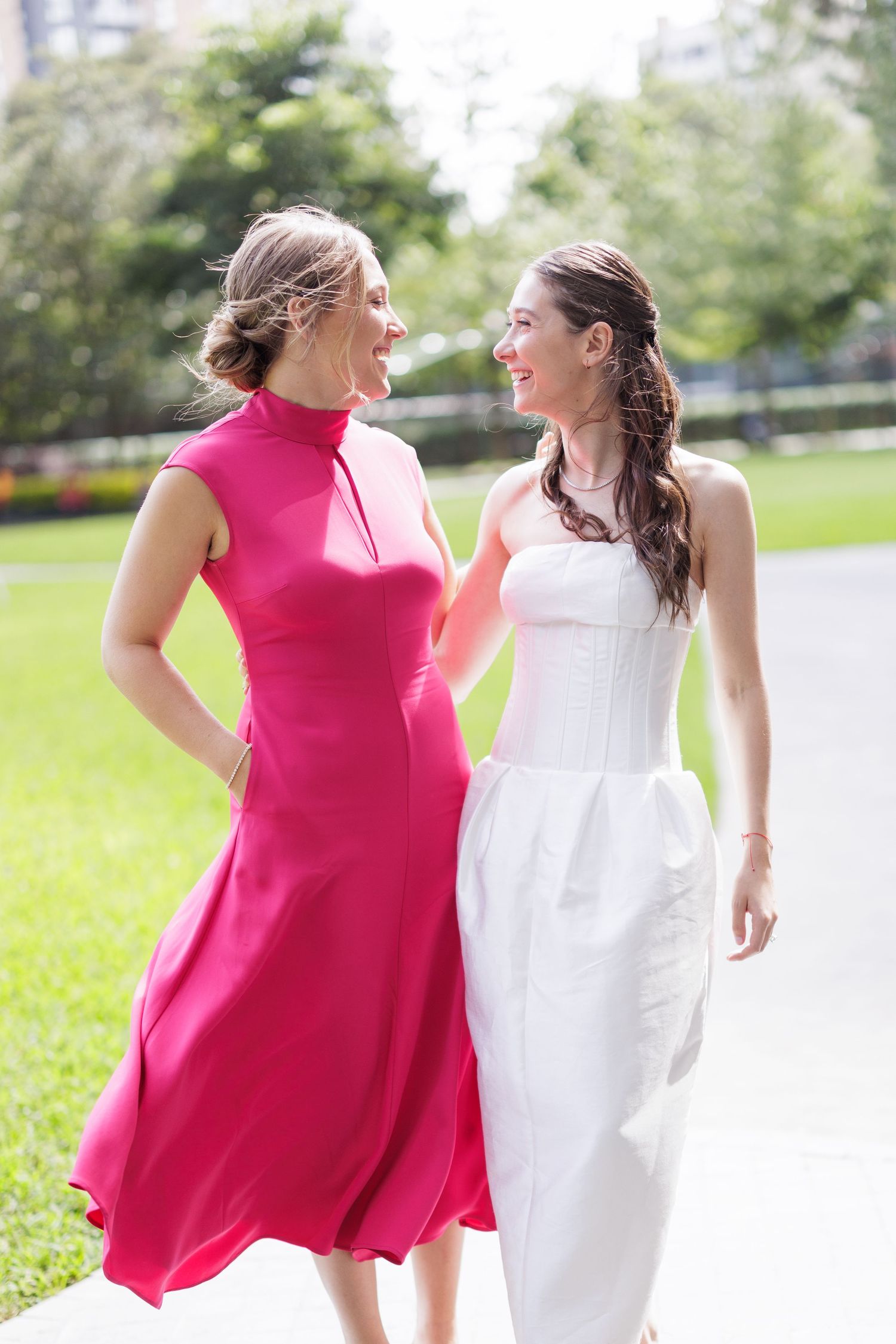 Women in pink and white summer dresses walking together outdoors on green grass.