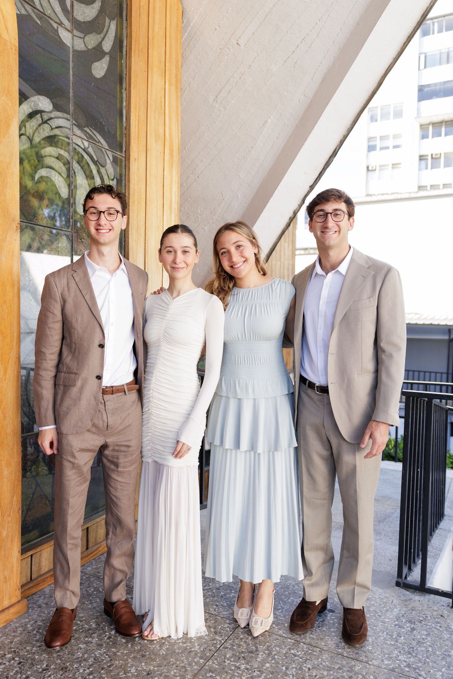 Wedding party in light blue dresses and tan suits pose together in a modern venue.