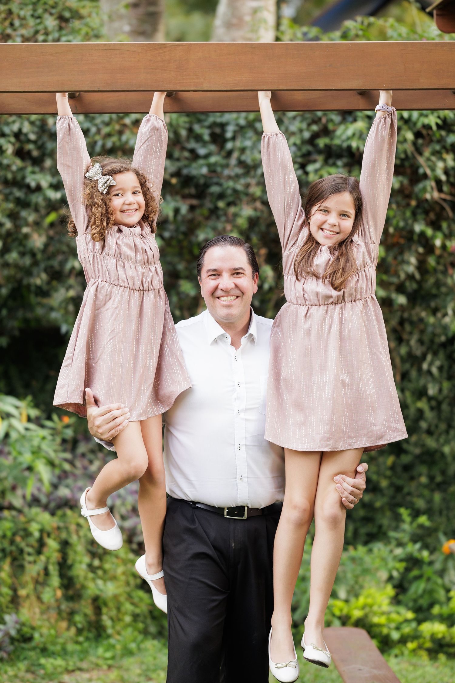 Playful family moment captured on wooden bench in garden with matching pink outfits.