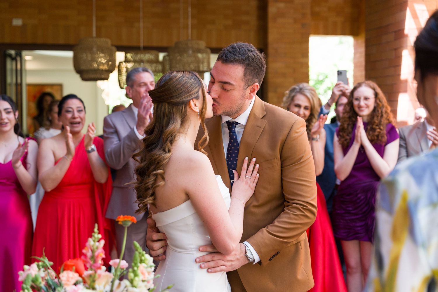 Wedding guests and newlyweds celebrating in a warmly lit brick-walled reception venue.