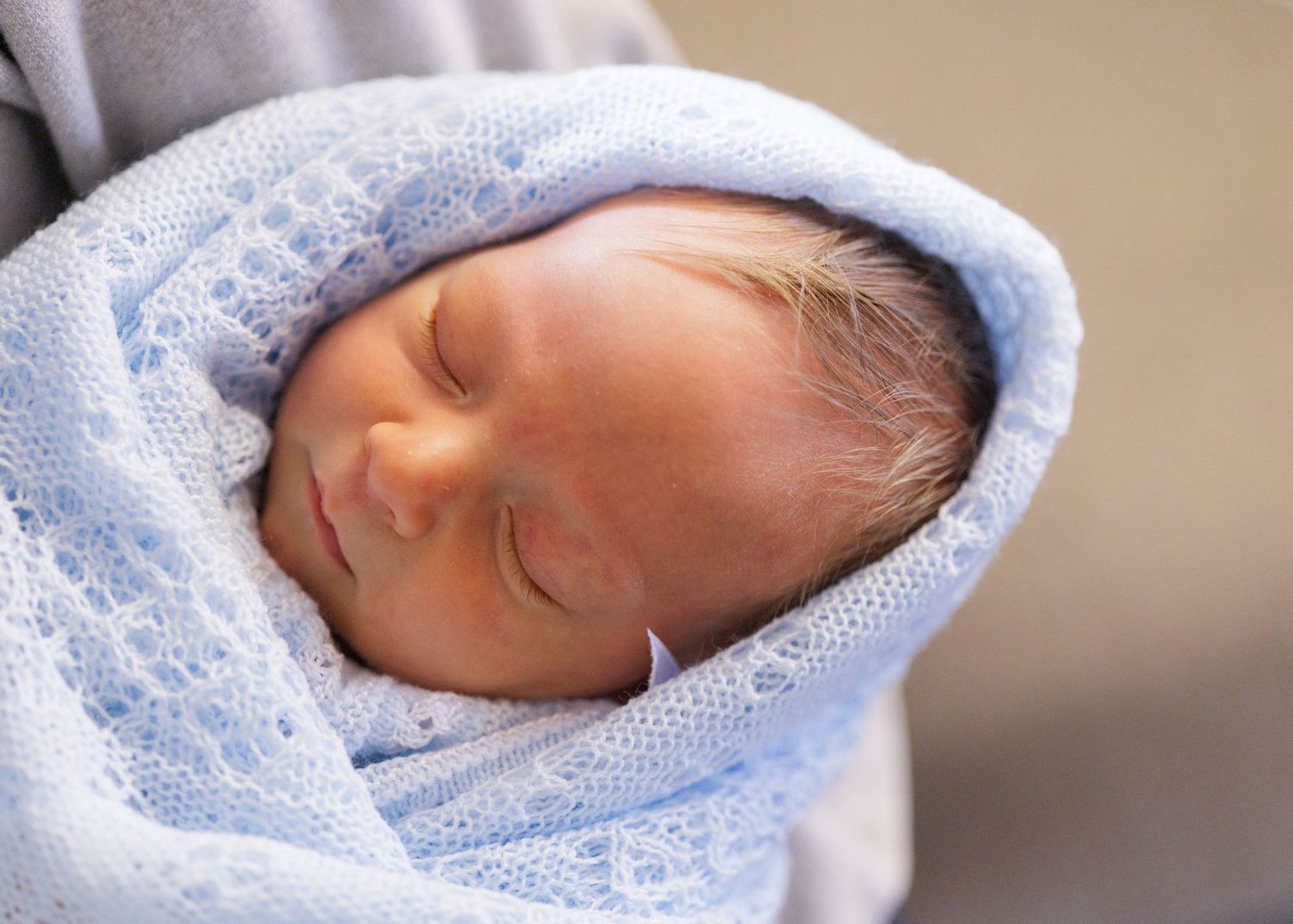 Newborn baby sleeping peacefully wrapped in soft blue lace blanket.