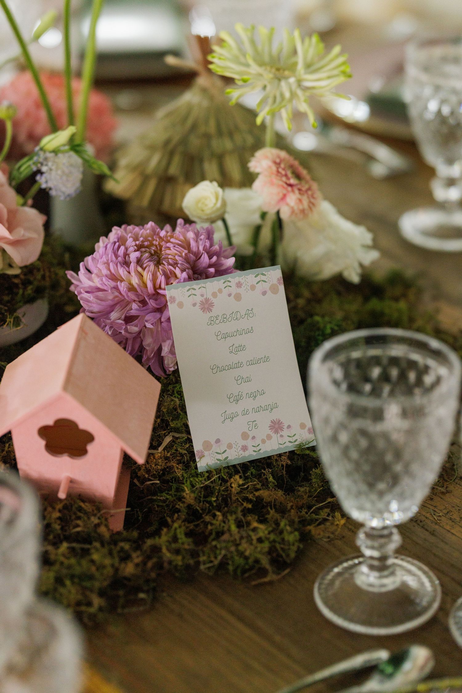 Elegant table setting with pink flowers, moss decorations and delicate place cards at a wedding reception.