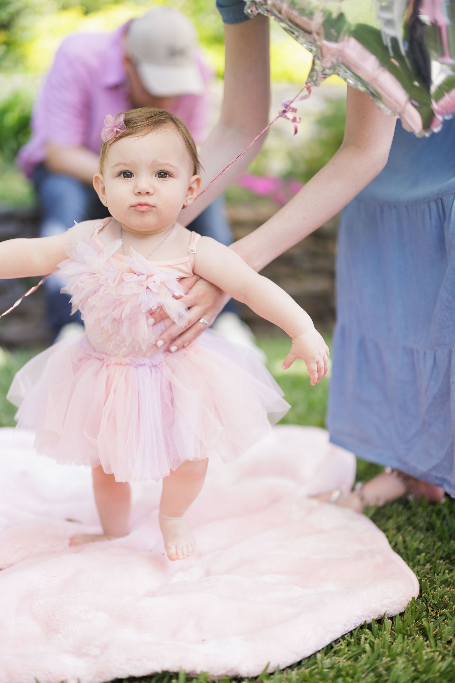 Baby in pink tulle dress sitting on grass during outdoor photo session.