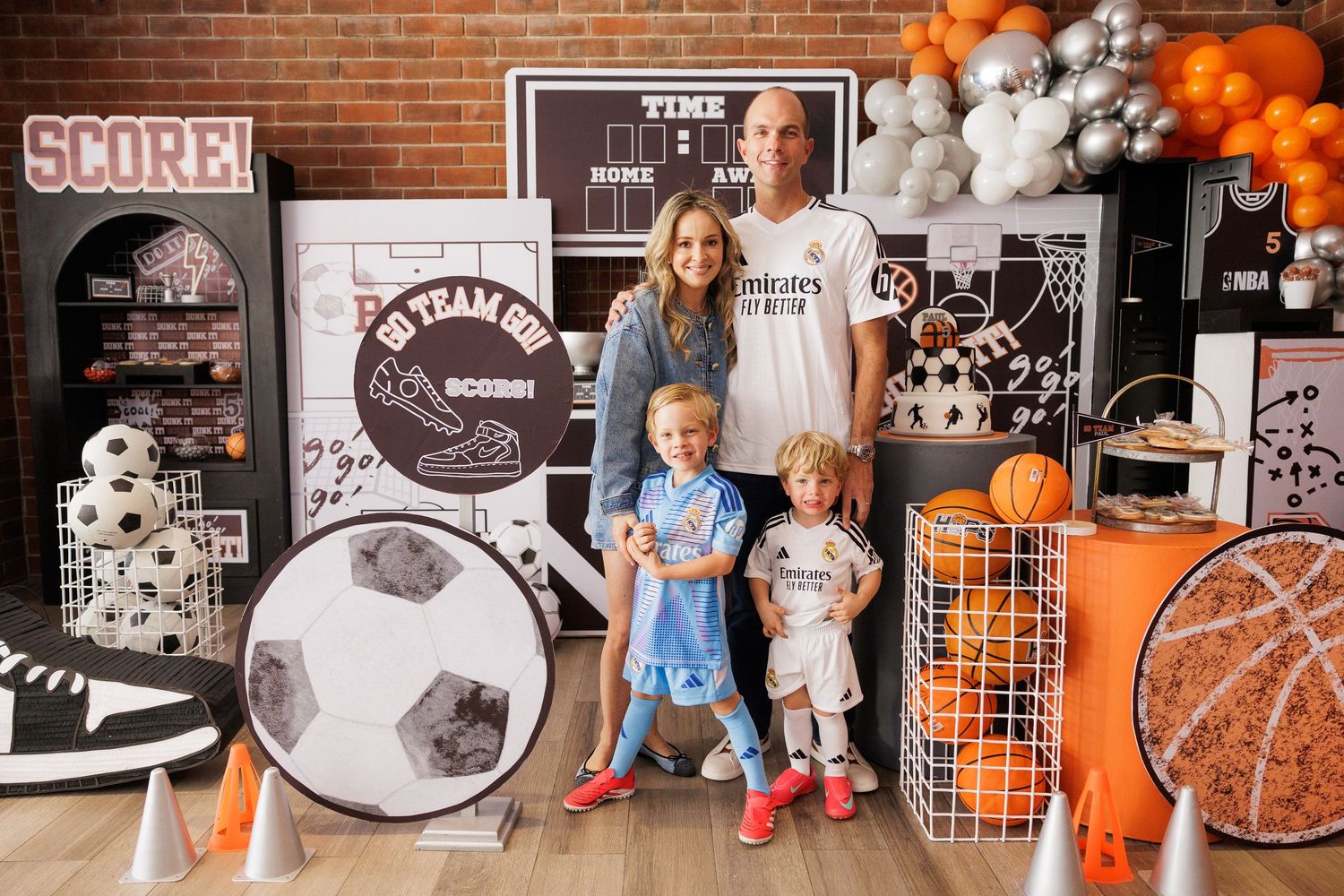 Sports-themed party setup with orange and white balloons against a brick wall backdrop.