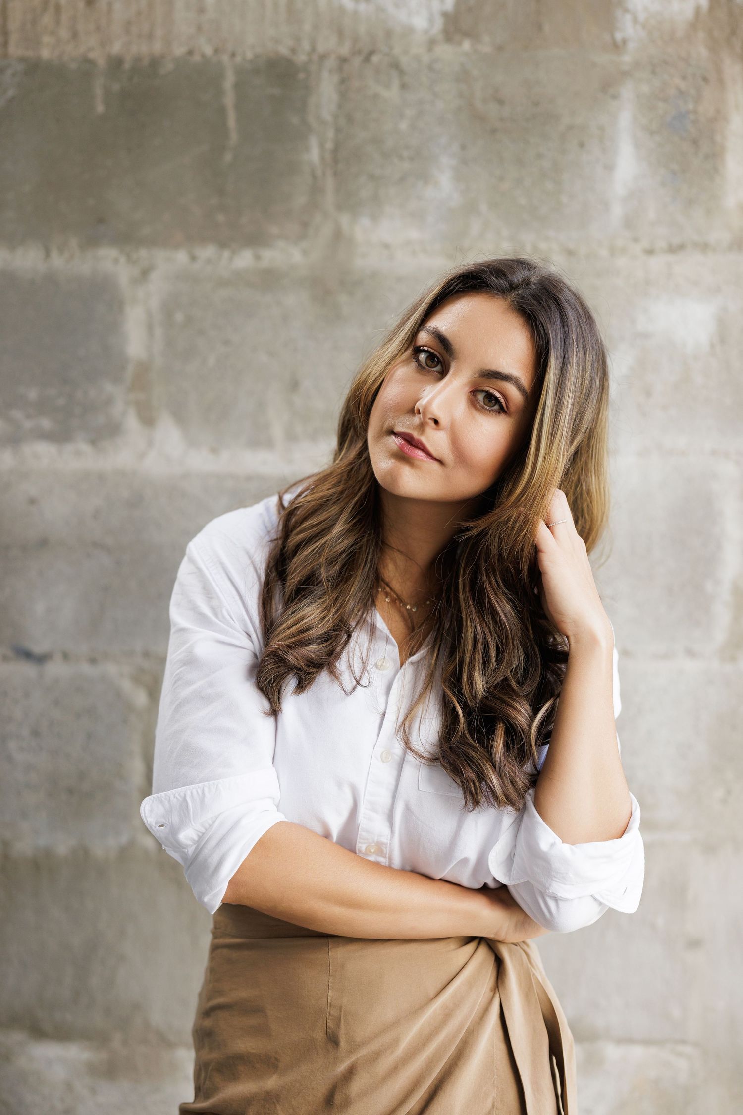 Professional portrait against concrete wall wearing white shirt and brown skirt.