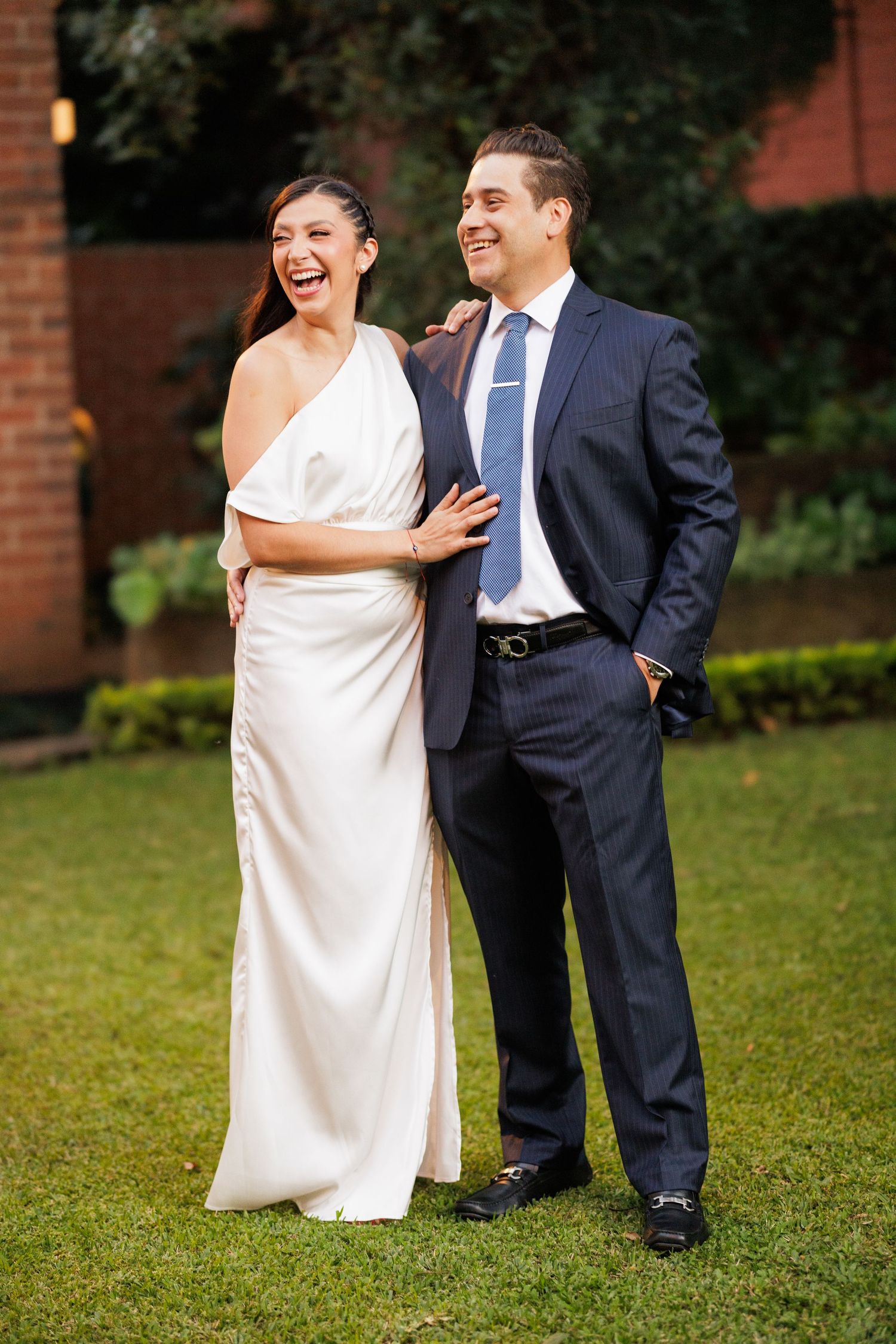 A couple laughs together on a grassy lawn during their wedding portraits.