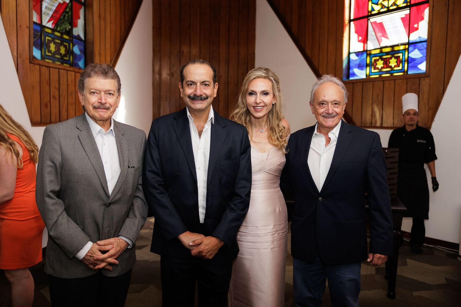 Wedding party members in formal attire pose together in front of stained glass windows at a church.