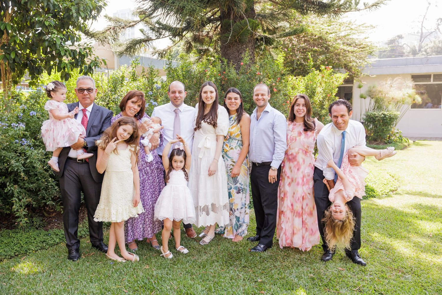 A large group poses together outdoors wearing coordinated pastel and white outfits.