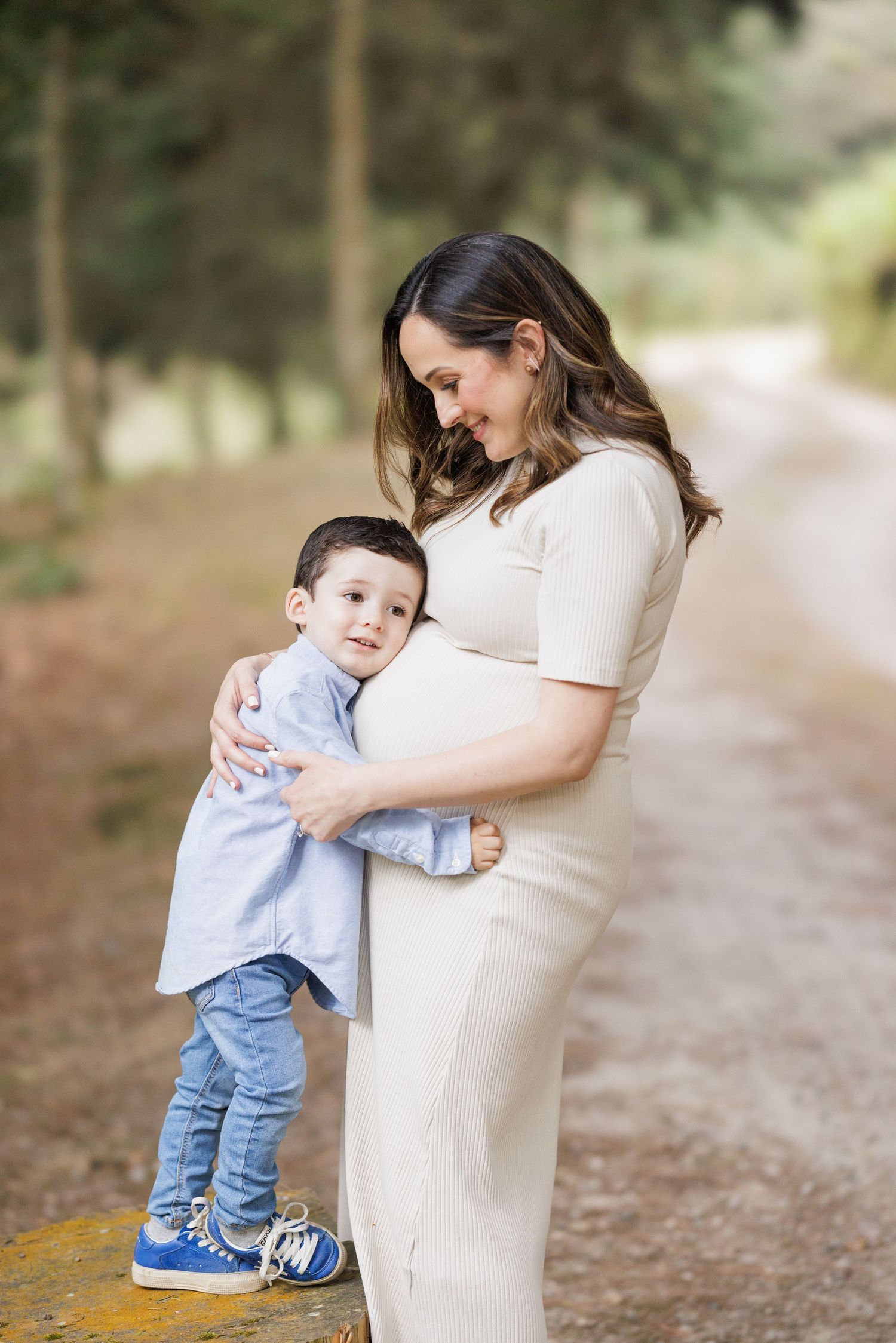 Young child hugging pregnant woman's belly in a touching outdoor moment.