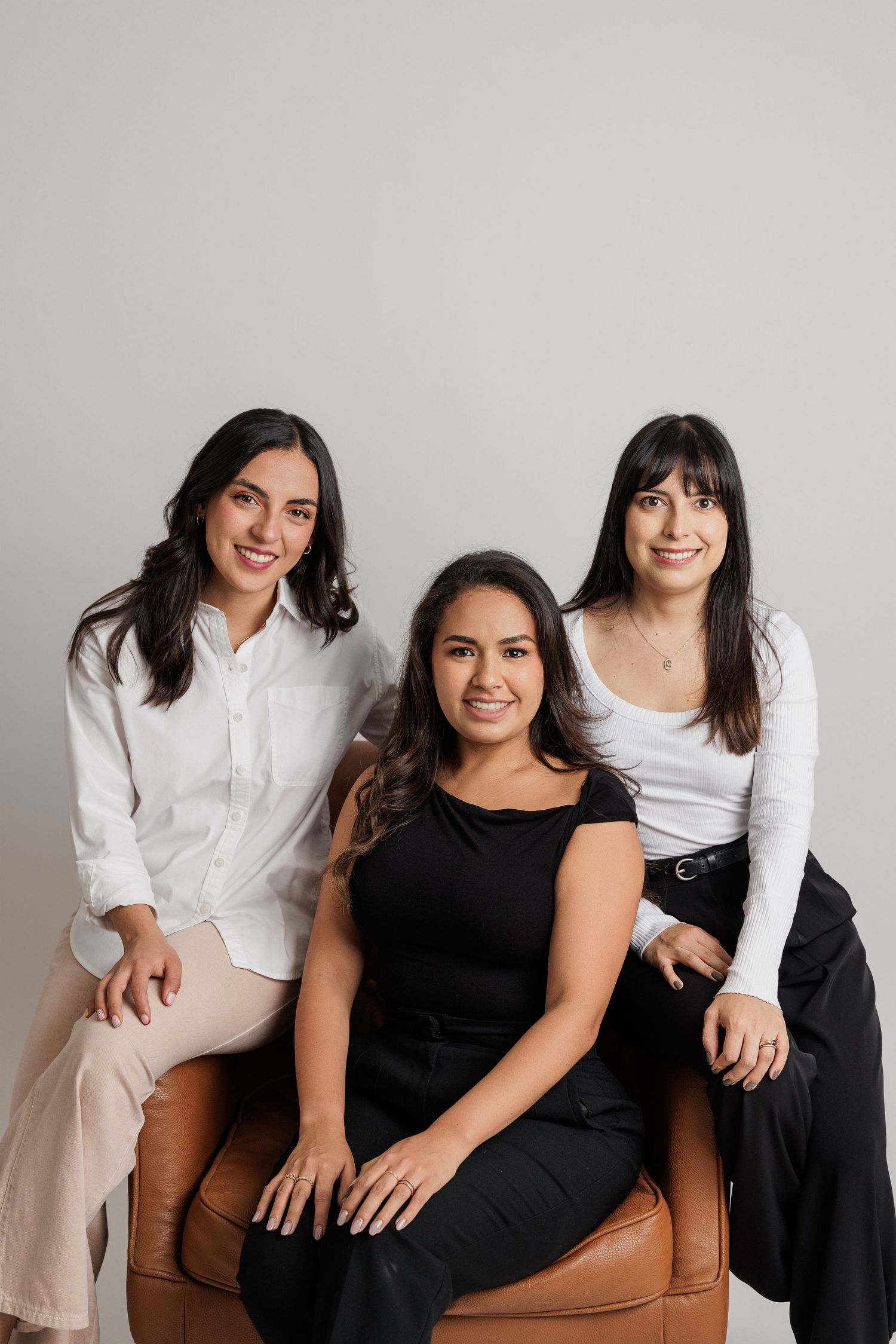 Casual group portrait with people wearing black and white outfits on brown leather furniture.