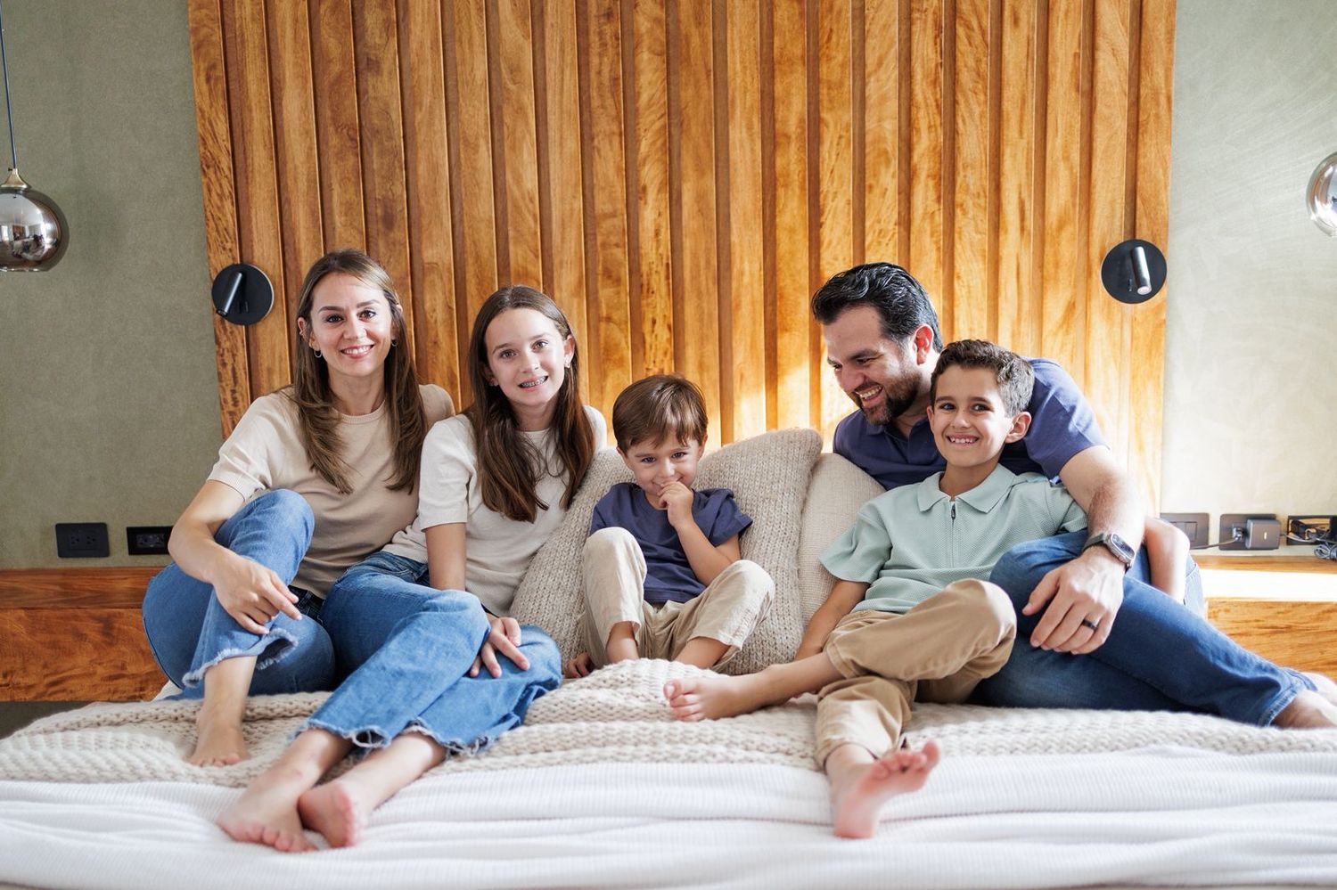 Family lounging together on a white bed in casual clothing.