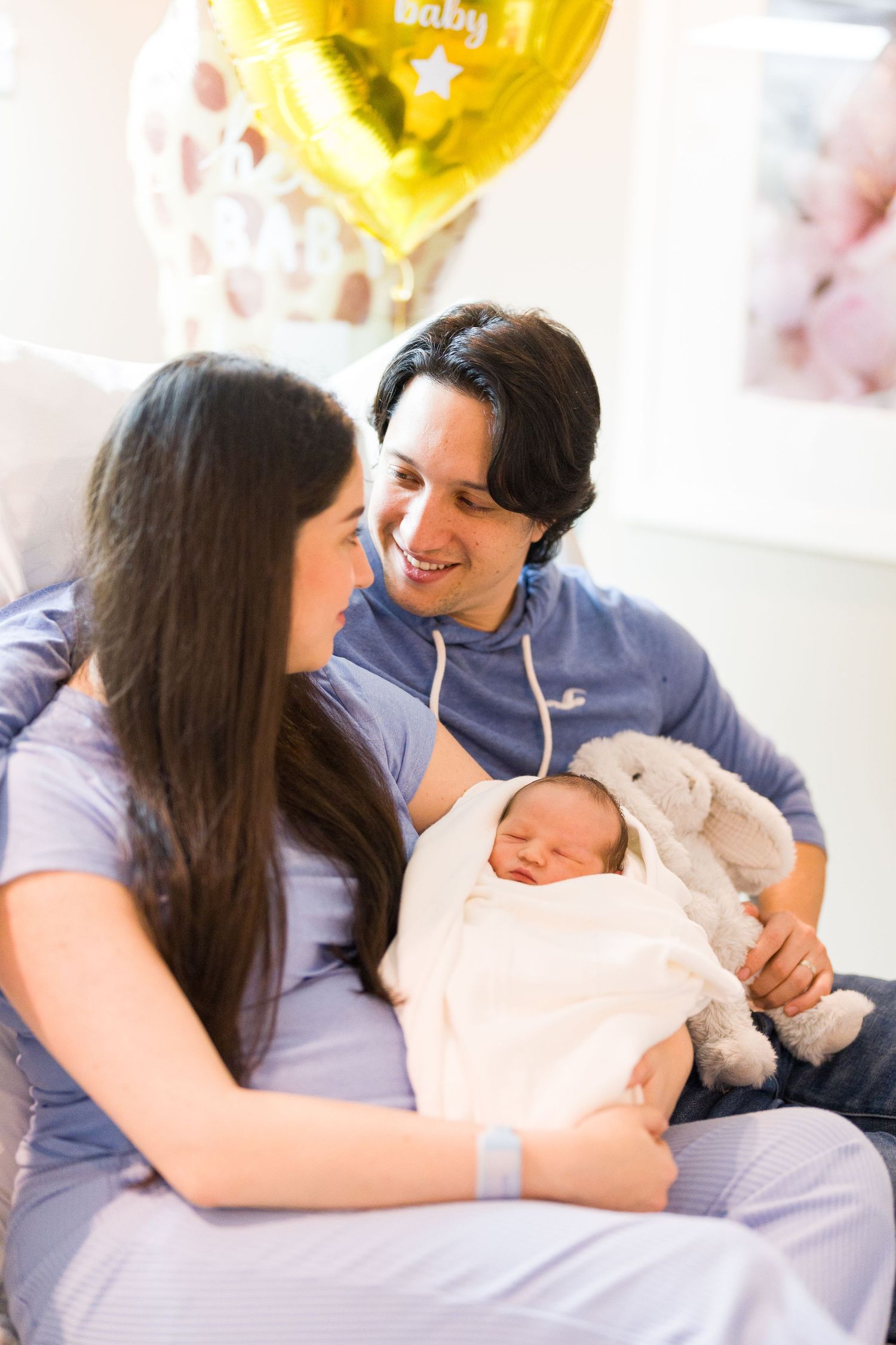 Parents share intimate moment with newborn baby under yellow balloon decorations.