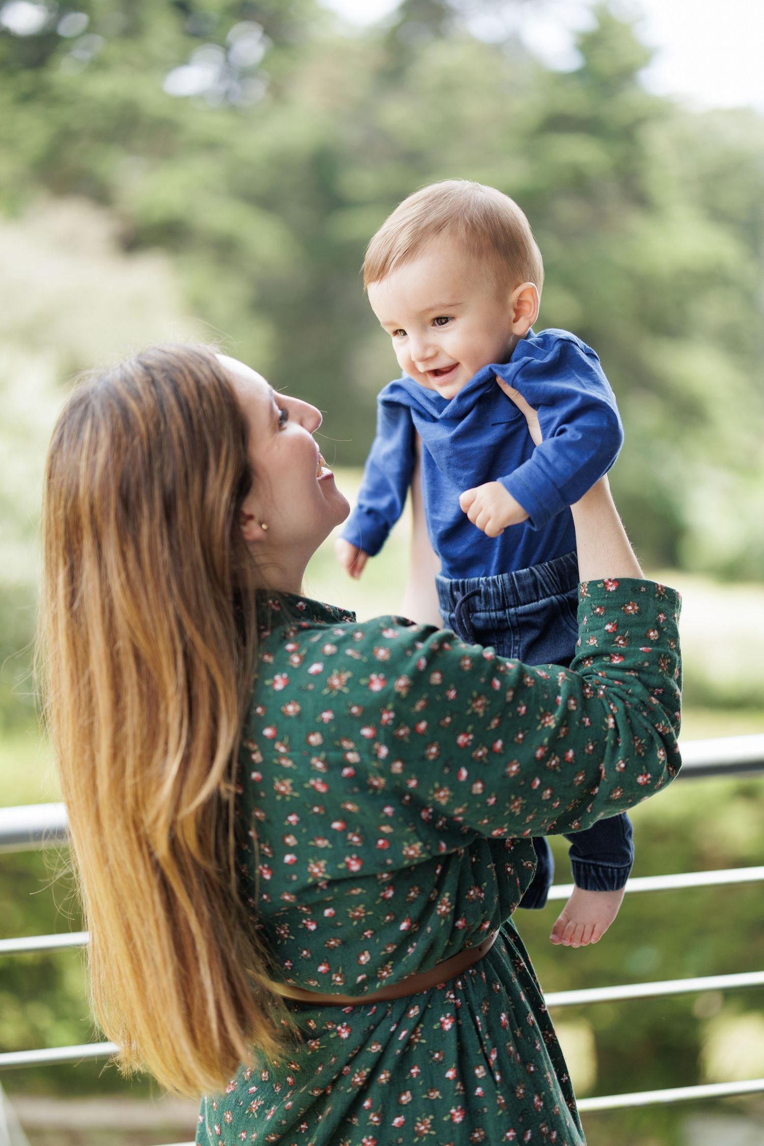 Parent and baby sharing playful moments outdoors against a green forest backdrop.