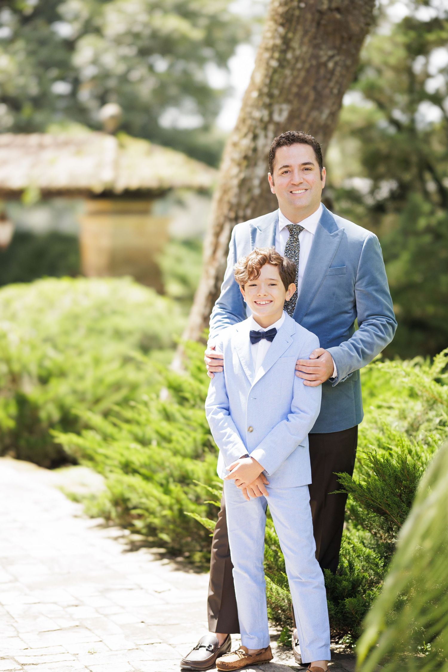 Two people in formal attire pose together in a lush garden setting.