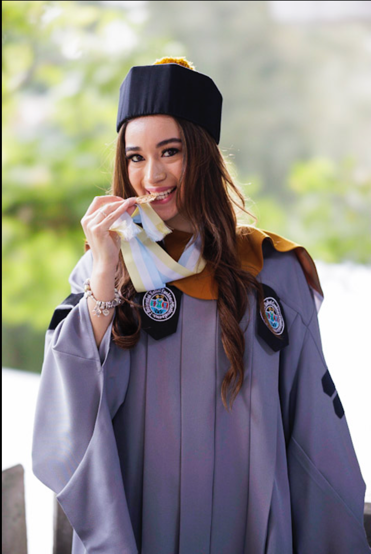 Graduate in academic regalia and black cap poses playfully with diploma.