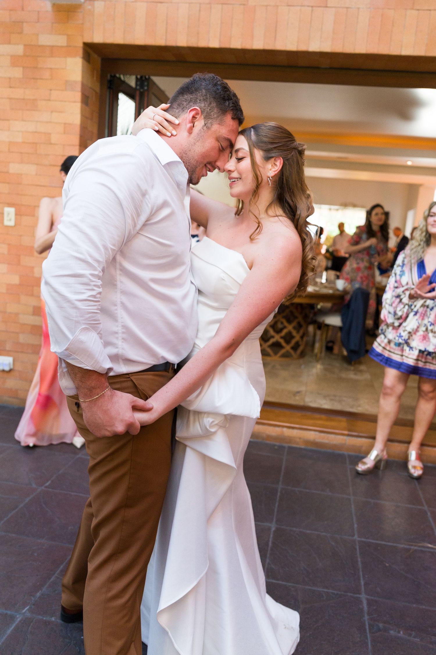 A couple shares a romantic dance dip moment on a dark tiled floor at their wedding reception.