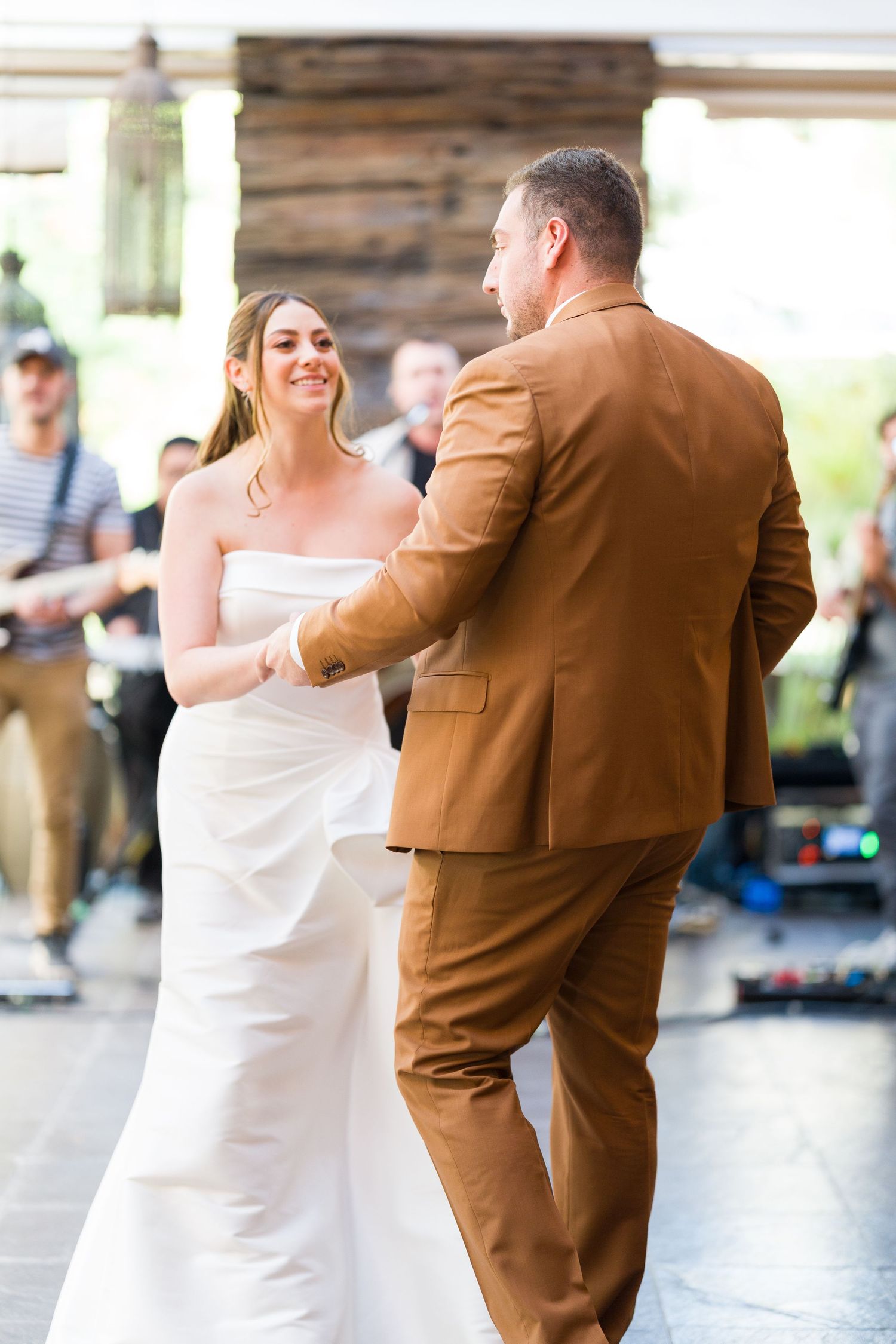 A couple performs their first dance at a rustic wedding venue with wooden walls.