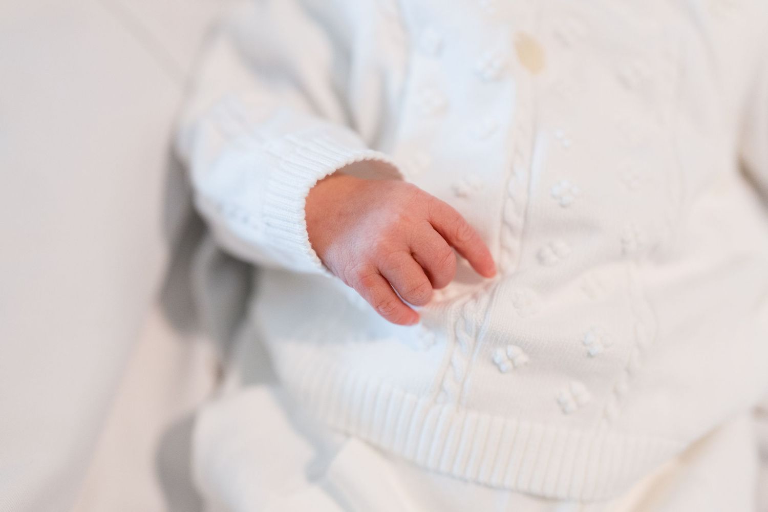Close up of newborn baby's tiny hand against white knit fabric.