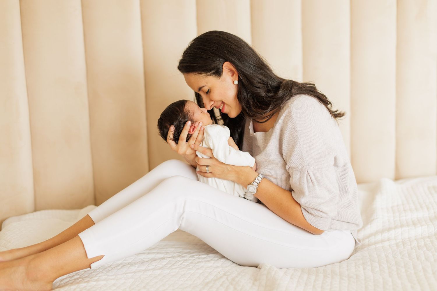 Mother and baby resting together on cream colored cushioned headboard.