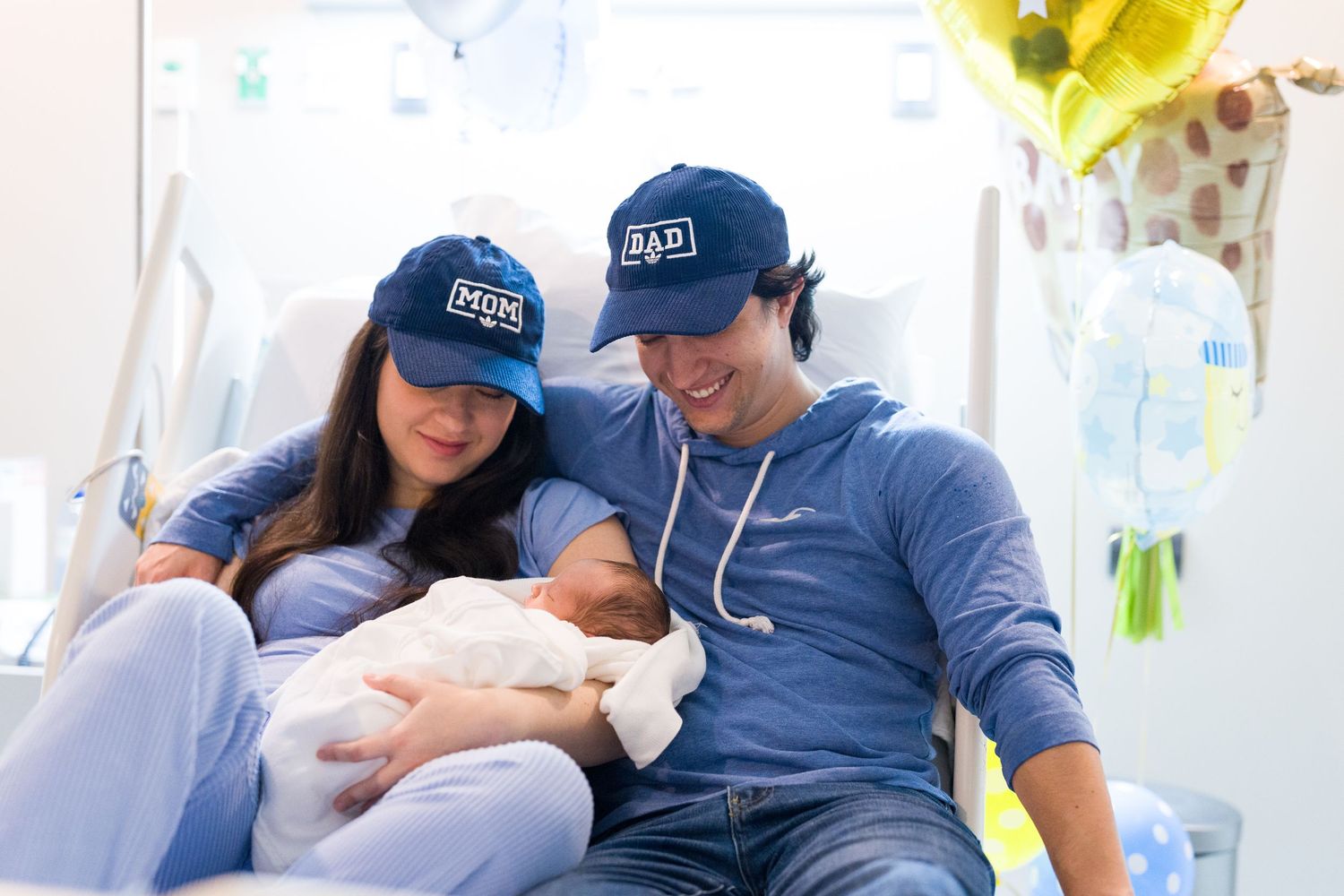 Parents in matching blue outfits share tender moment with newborn in bright room.