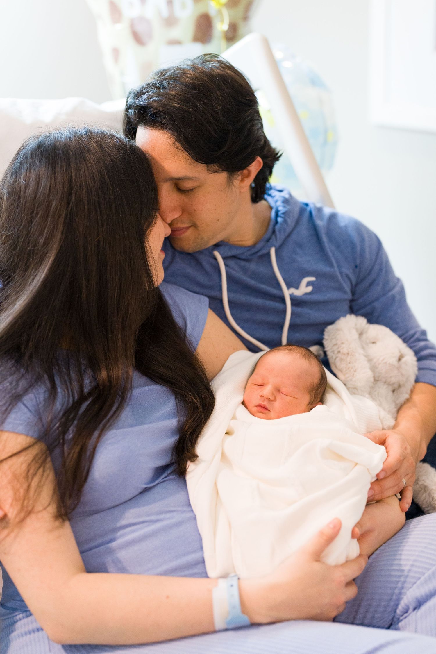 Intimate family moment as parents bond with their sleeping newborn baby in soft lighting.