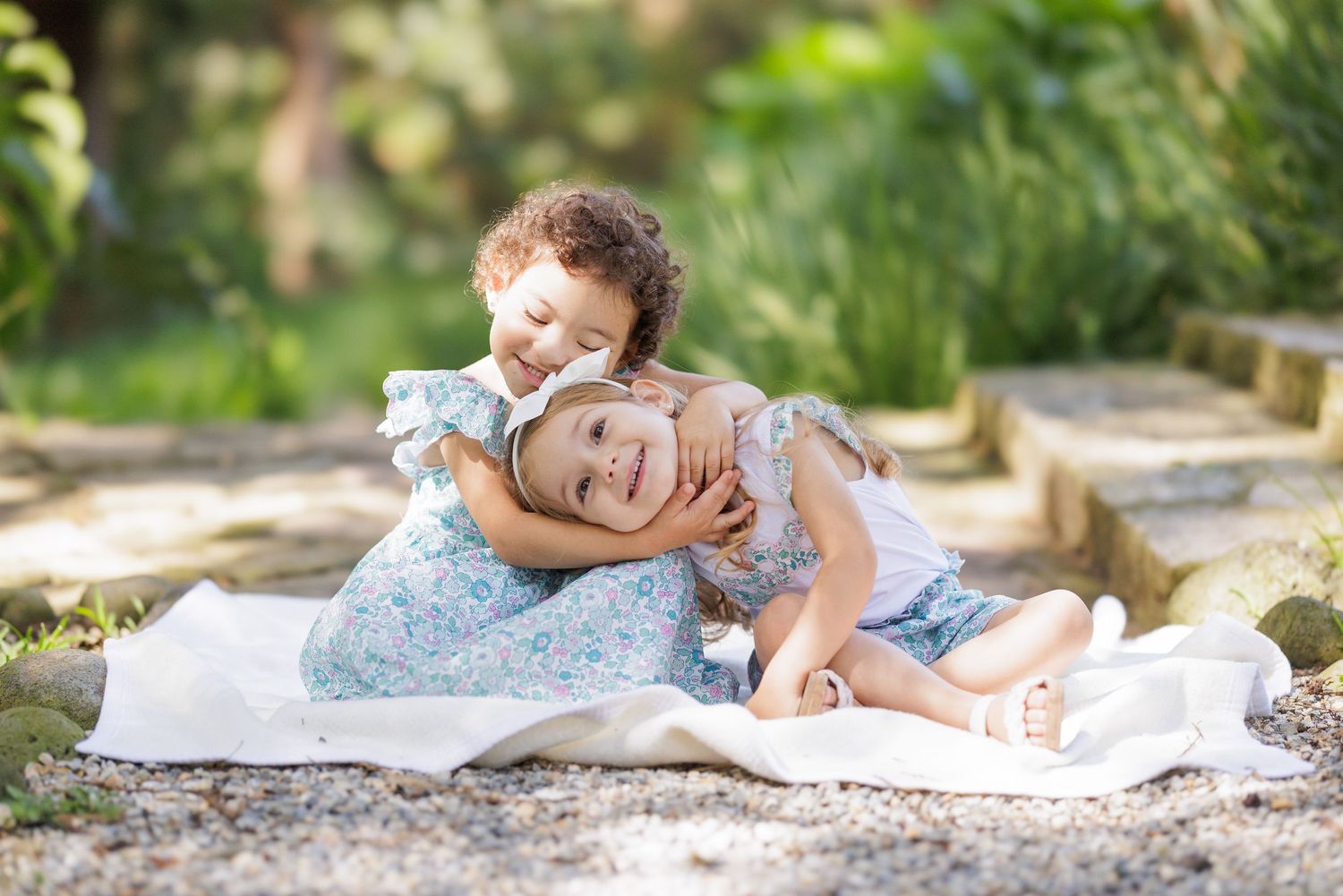 Children in floral dresses lay on blanket outdoors during summer photoshoot.