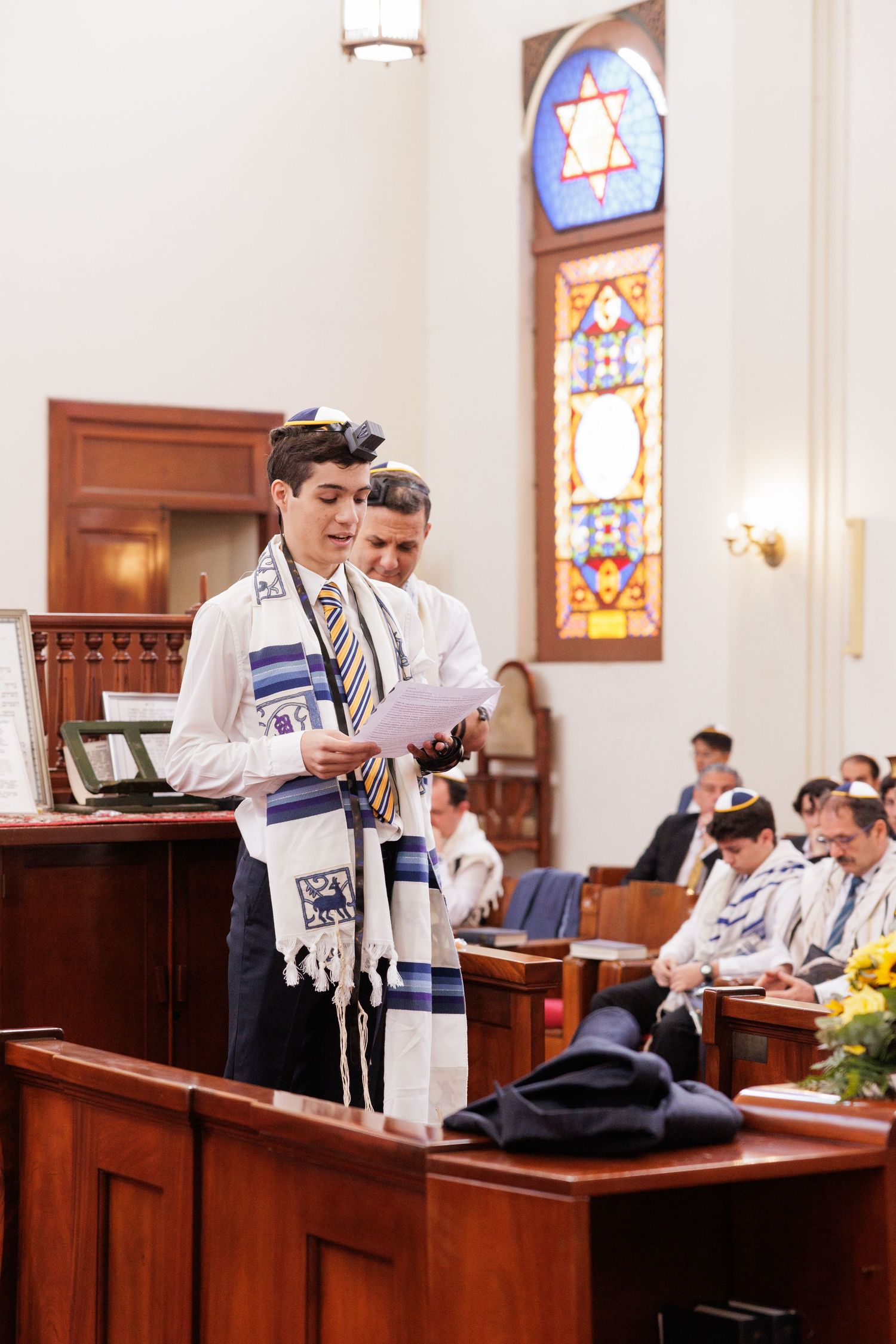 People in prayer shawls reading from religious texts at wooden podiums in a synagogue.
