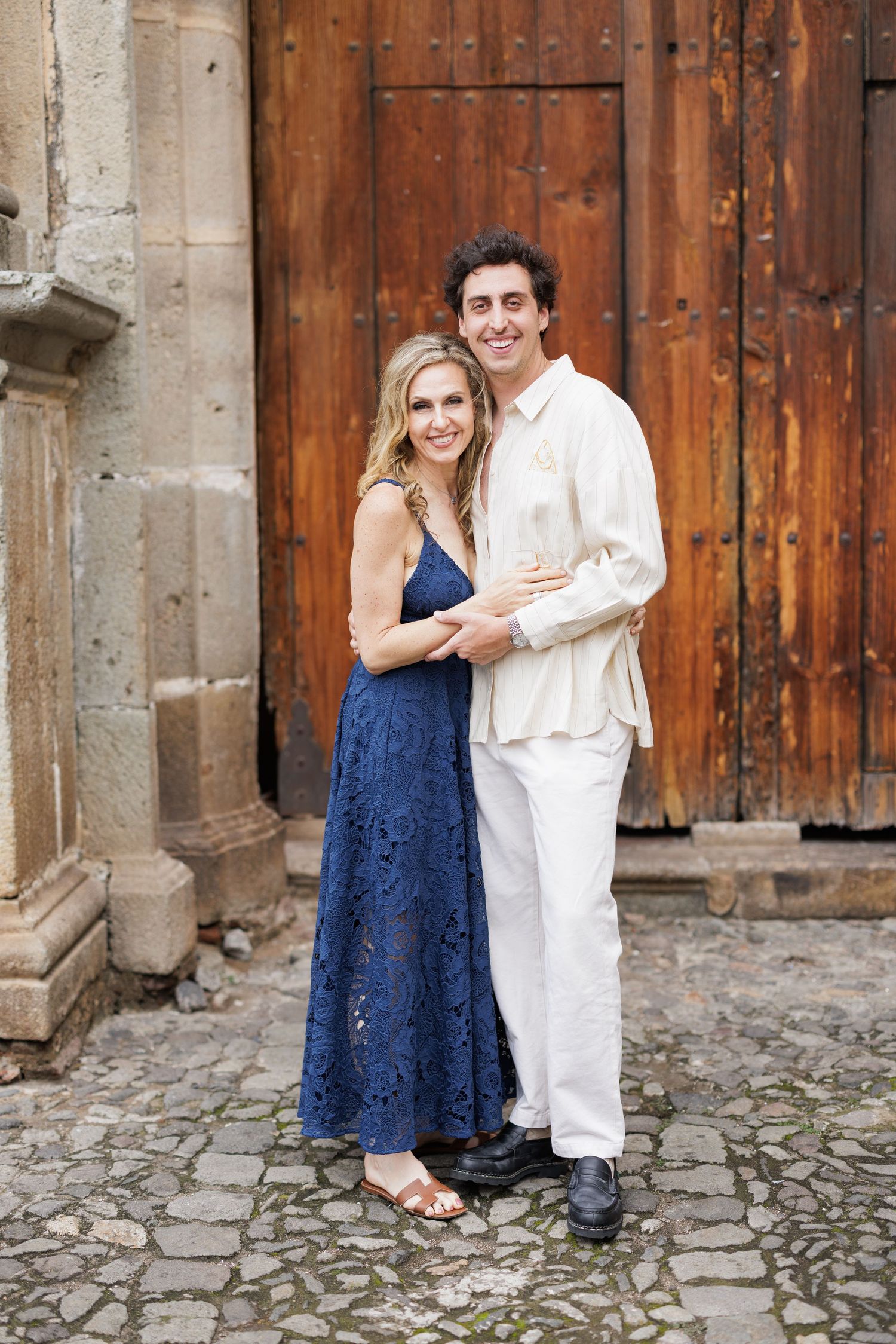 A couple poses in formal attire against a rustic wooden door at a historic venue.