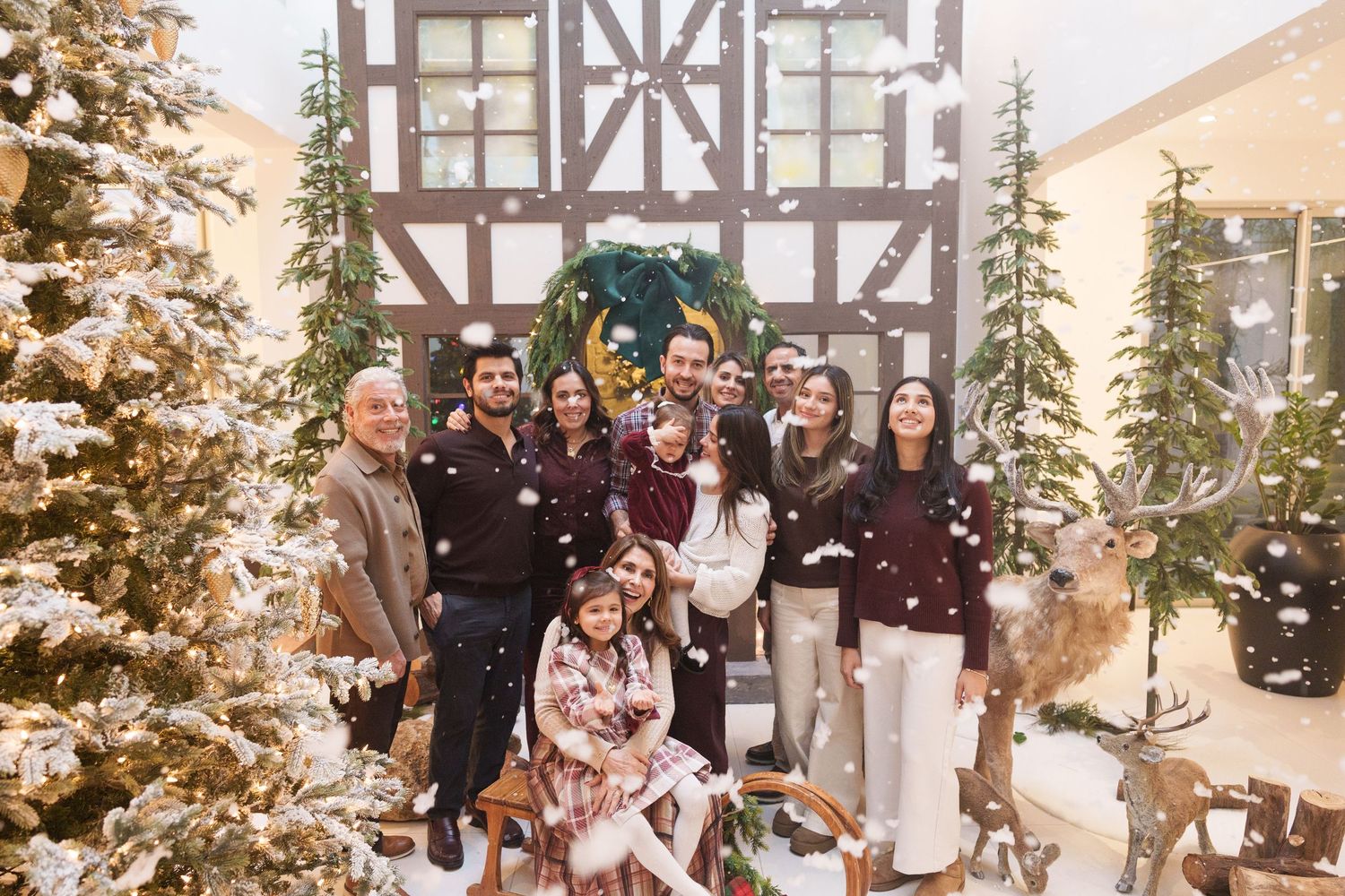 Holiday family gathering in front of decorated Christmas trees and Tudor-style home interior.