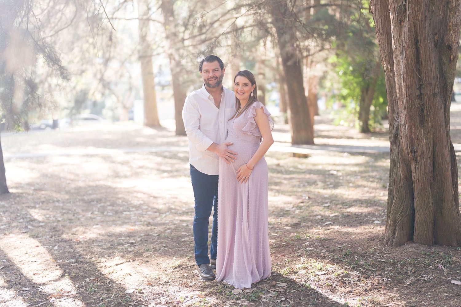 Maternity photo session in a sunlit forest with soft natural lighting.
