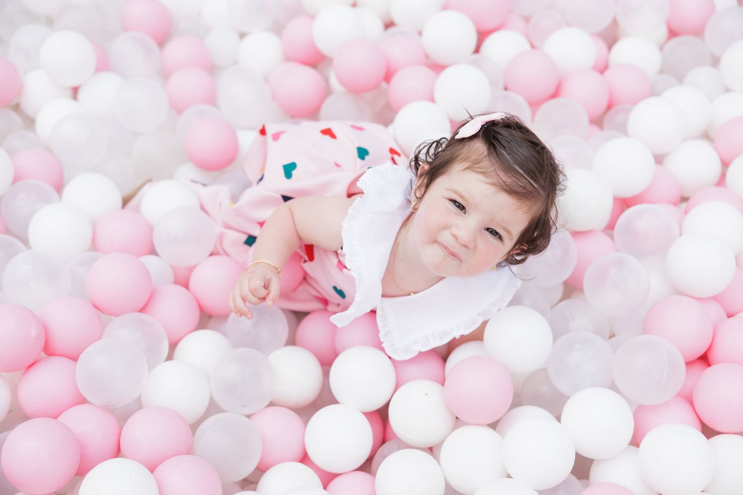Child laying in a ball pit filled with pink and white balls.