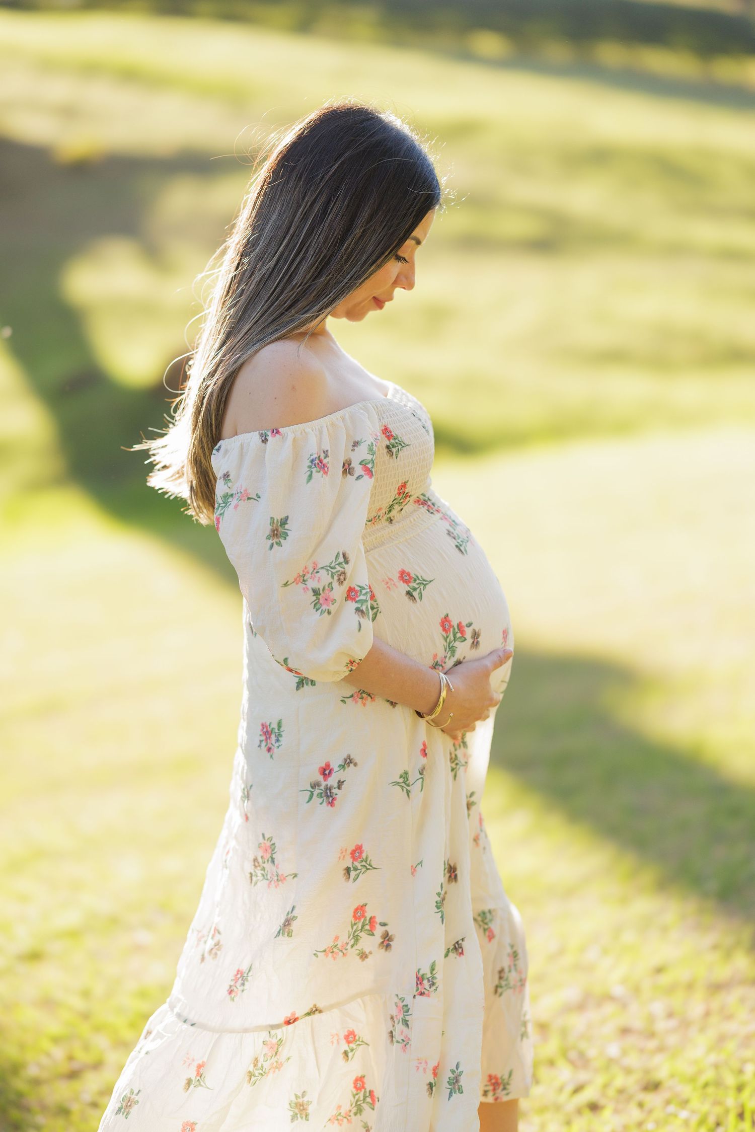 Woman in a white floral dress walking through a sunlit garden.