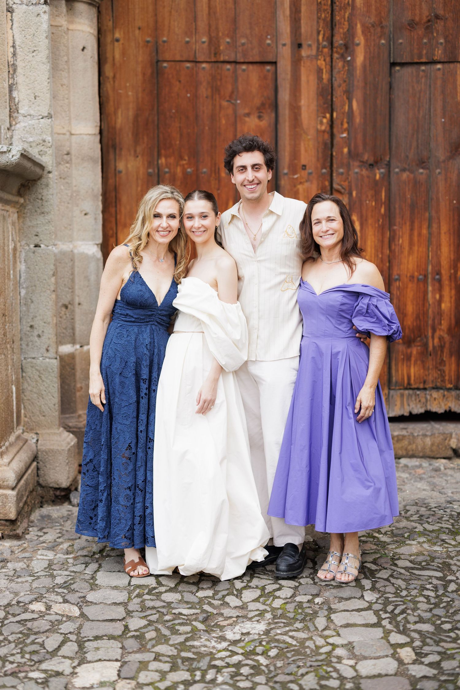 Wedding party members pose together in coordinated blue and white formal attire against wooden doors.